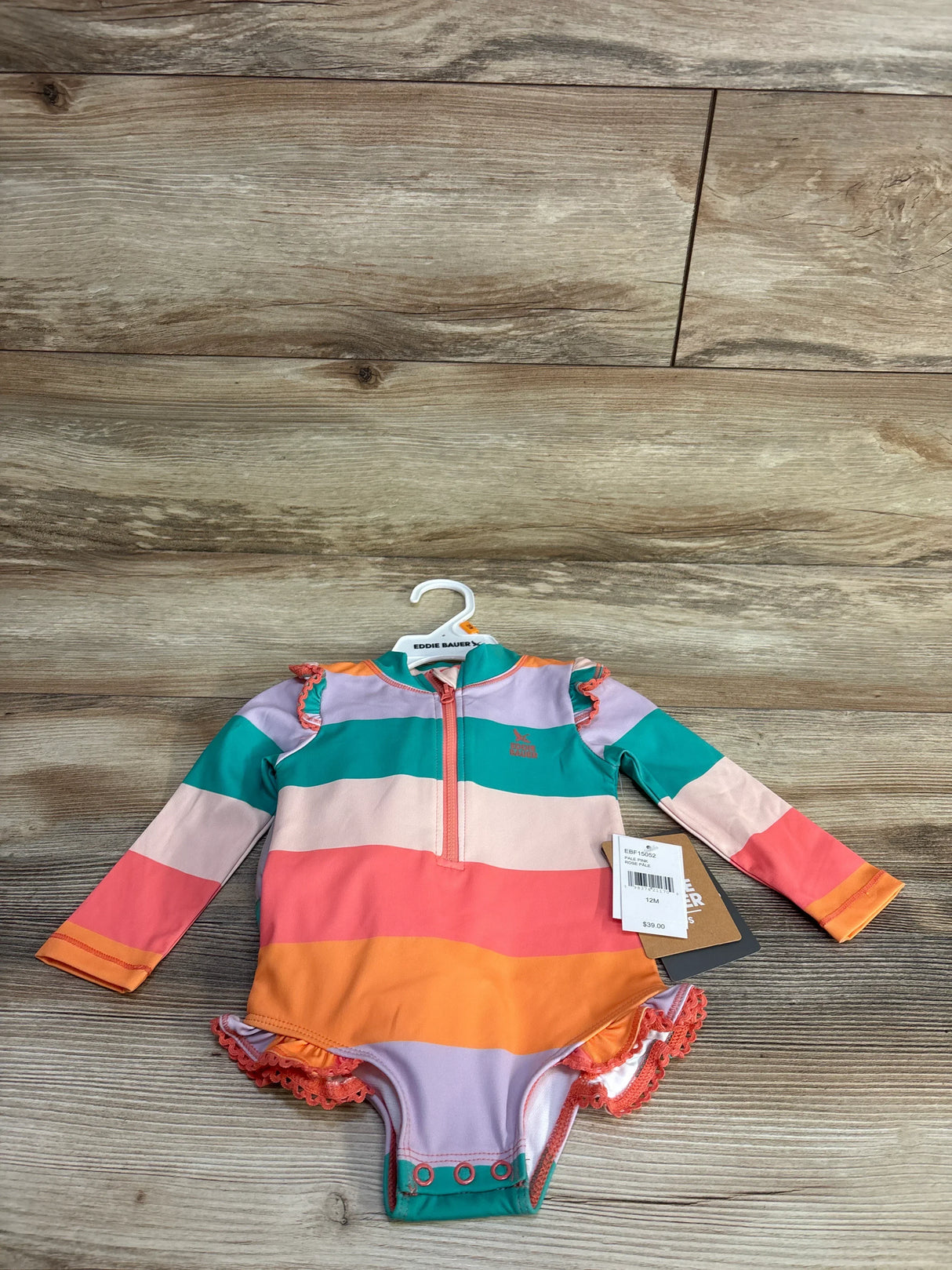 Top-down view of girls' one-piece rashguard swimsuit by Eddie Bauer with wide colorful stripes and front zipper on wood floor