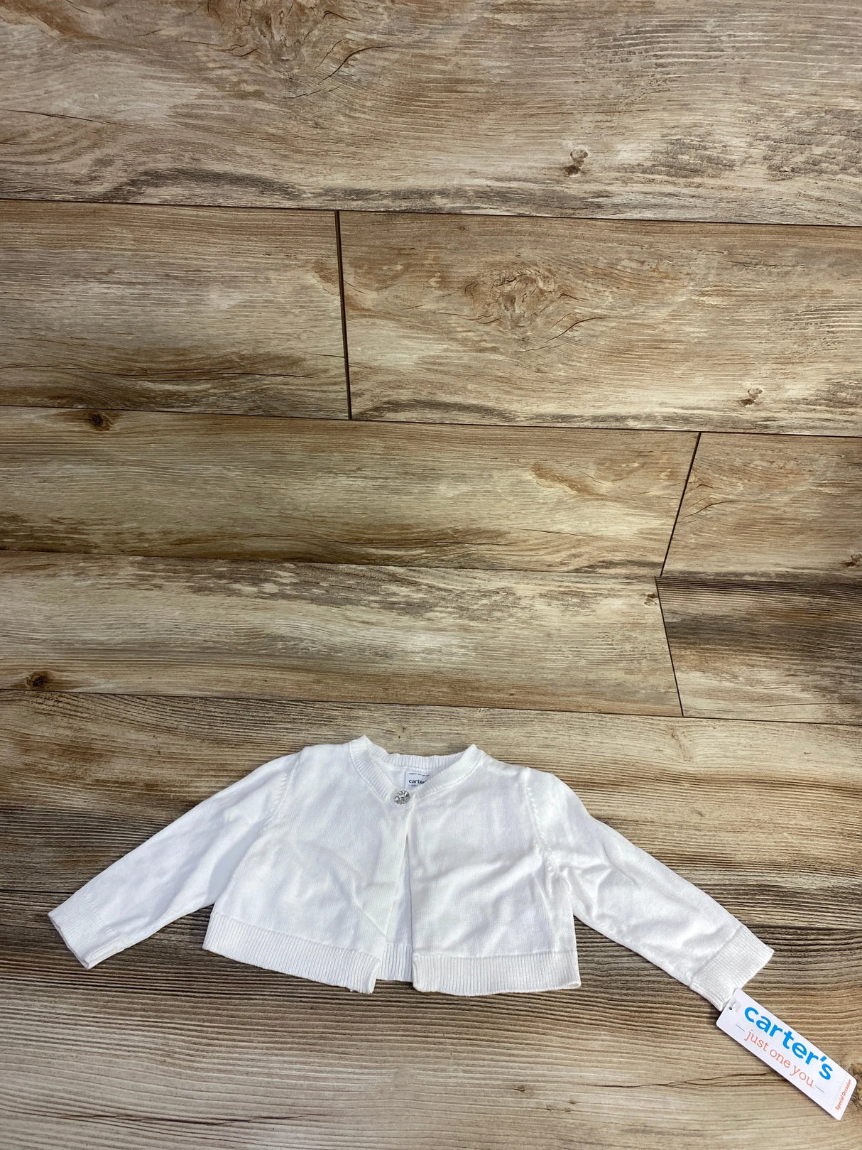 White baby cardigan with single decorative button, Carter's brand tag, on wood background