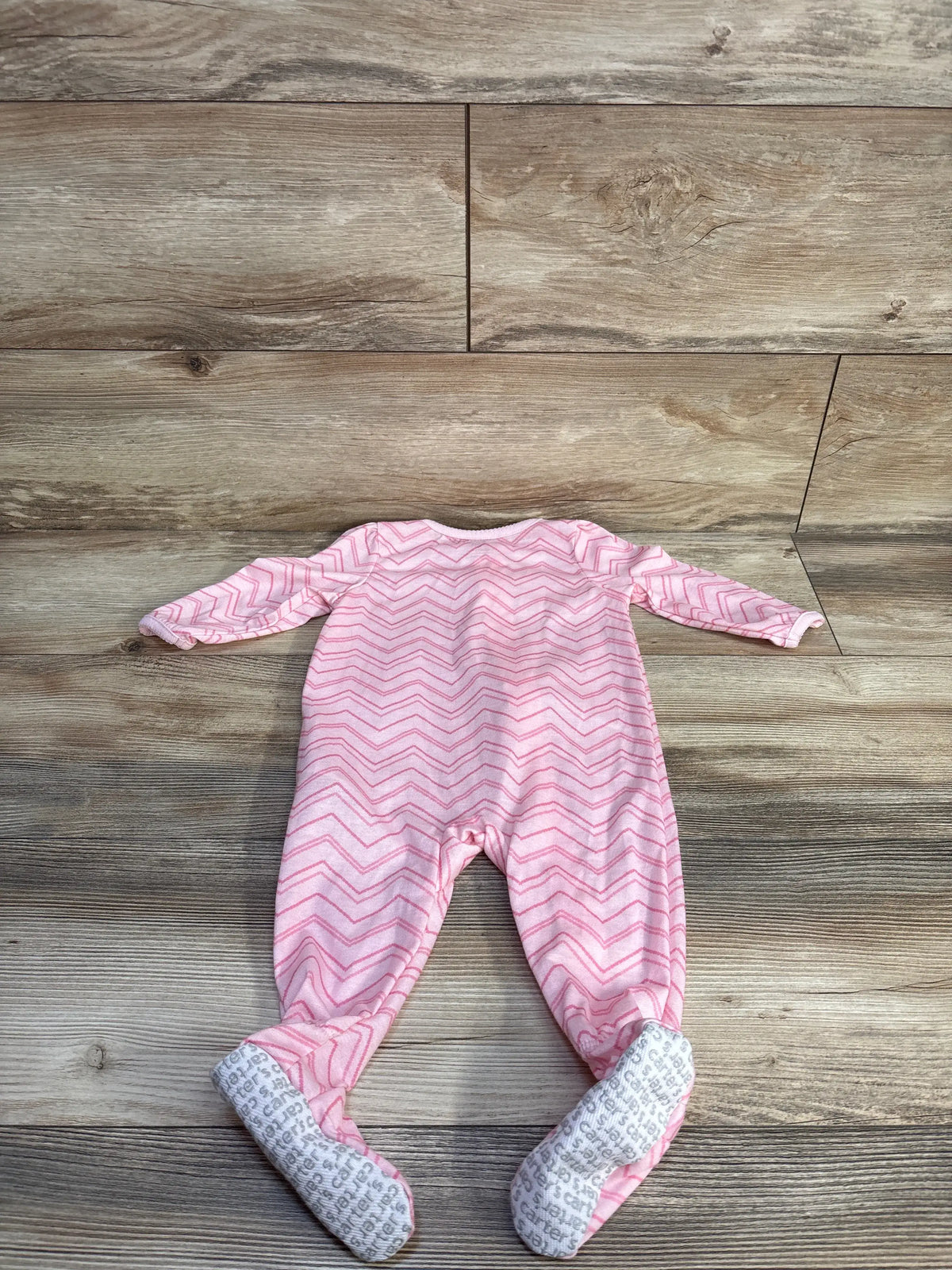 Front view of a pink Simple Joys baby sleeper showcasing chevron pattern and covered feet on a wood-patterned background