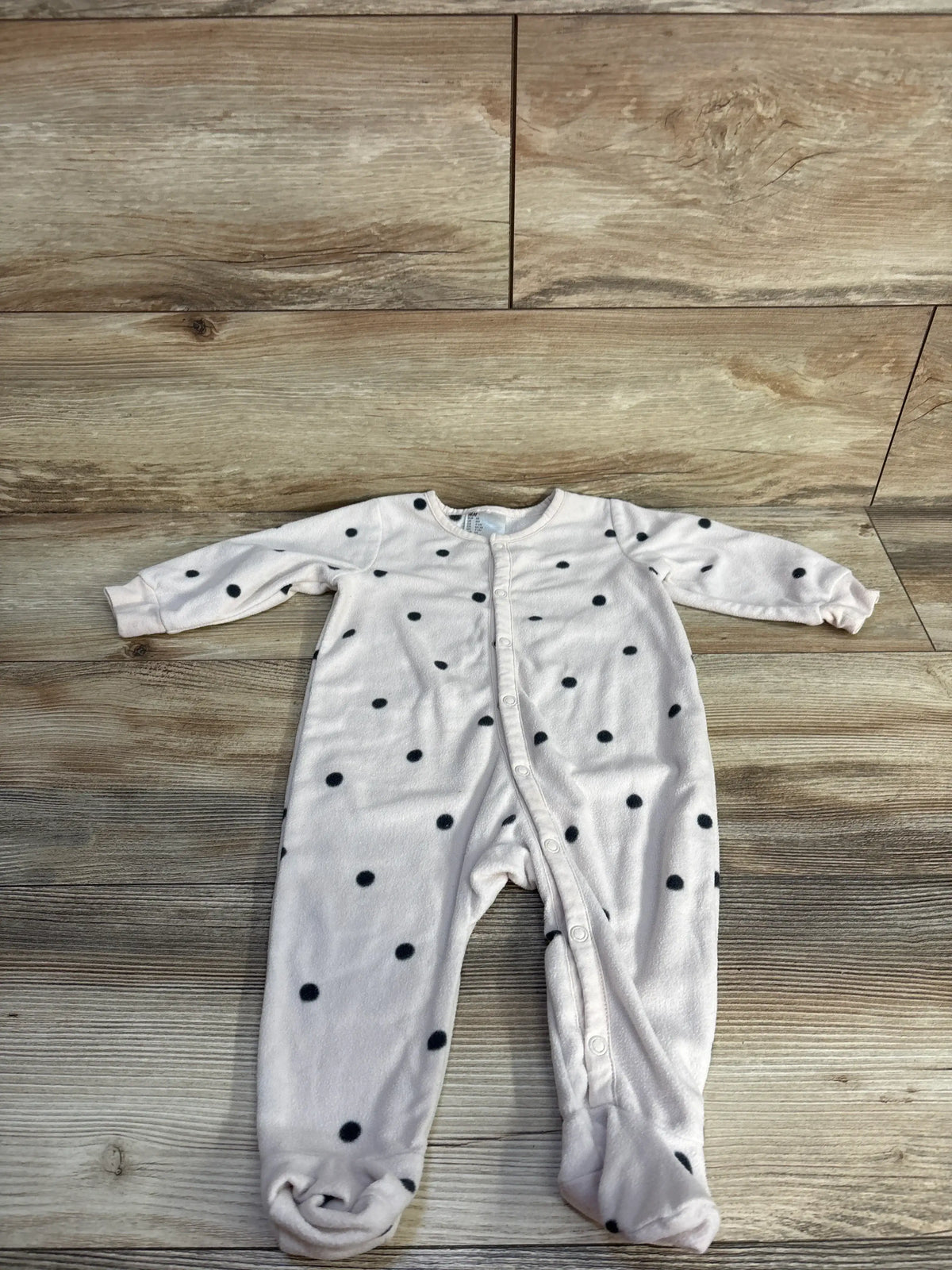 Front view of H&M beige polka dot sleeper showcasing long sleeves, footed legs, and snap front on a wood plank background