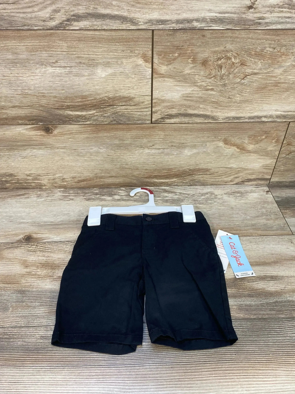 Front view of Cat & Jack black 4T uniform shorts showing button waist, belt loops and side pockets on wood background