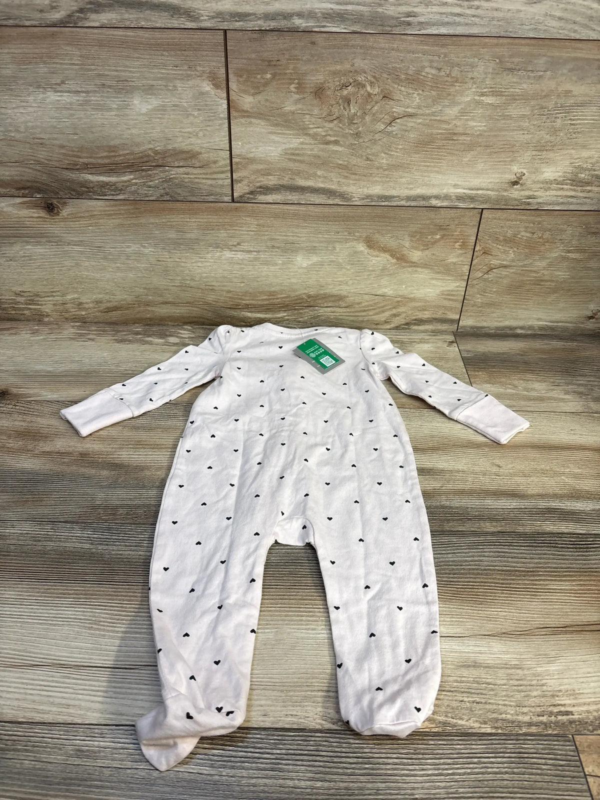 White baby footed sleeper with small black heart pattern, long sleeves, on wood floor