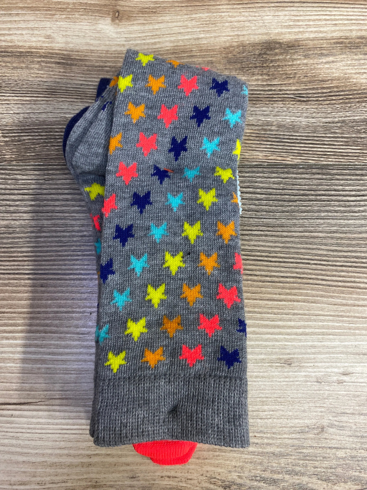 Flat lay of folded grey knee socks with multicolor butterfly print and orange toe accent on wood plank floor