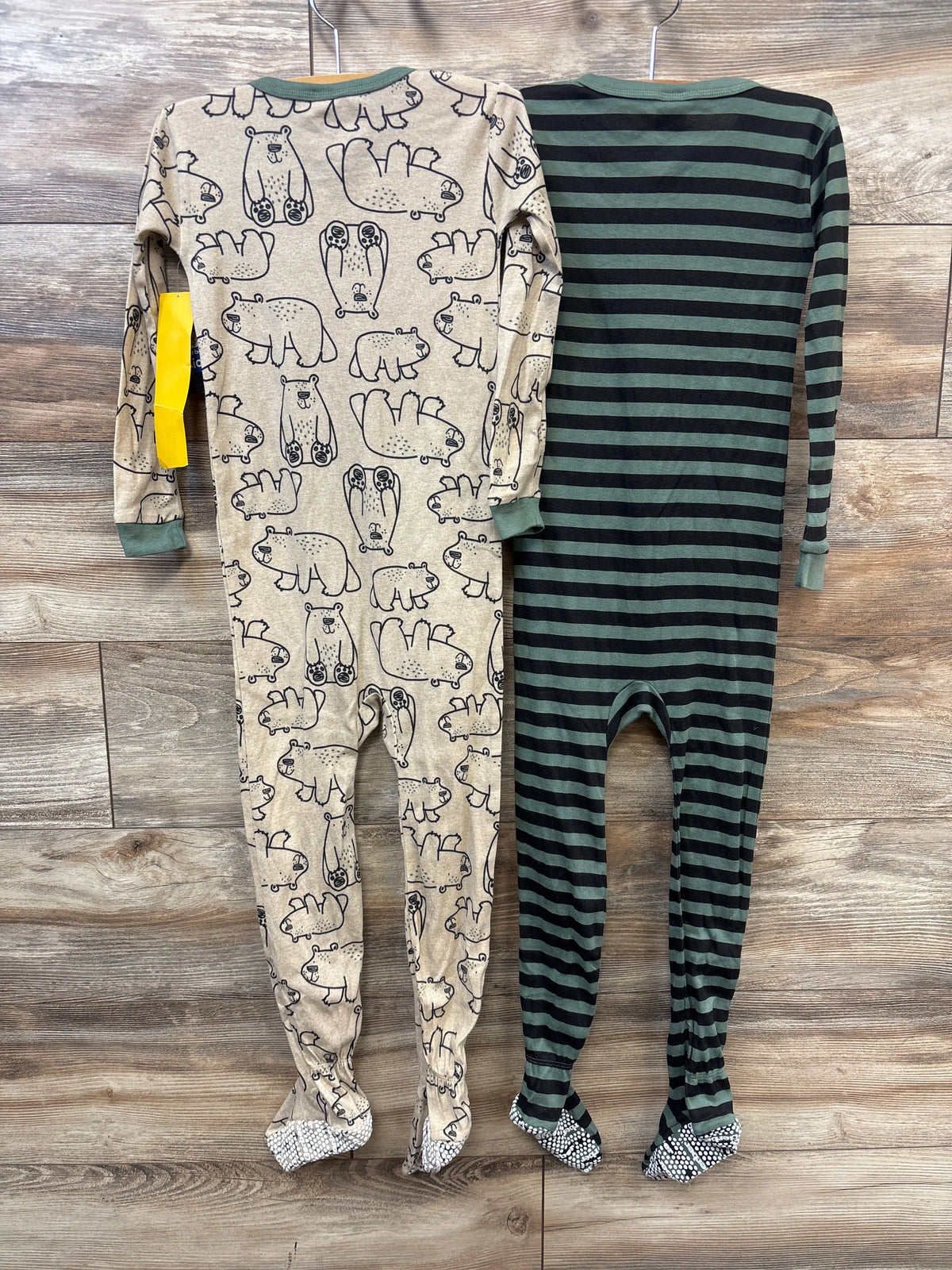 Front view of Gerber 2pk Sleep N Play sleepers showcasing animal print and green-and-black stripes on hangers over a wood floor