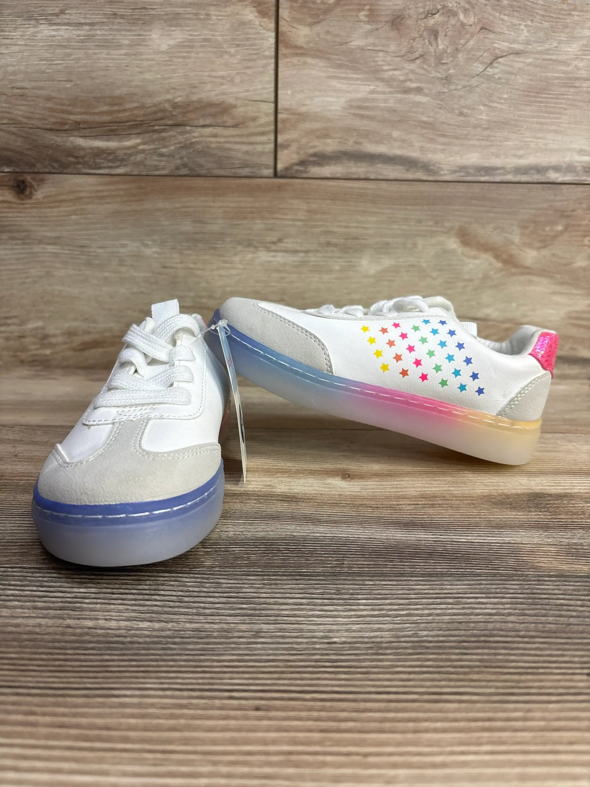 White kids sneakers with rainbow star design and translucent ombre soles on wood floor