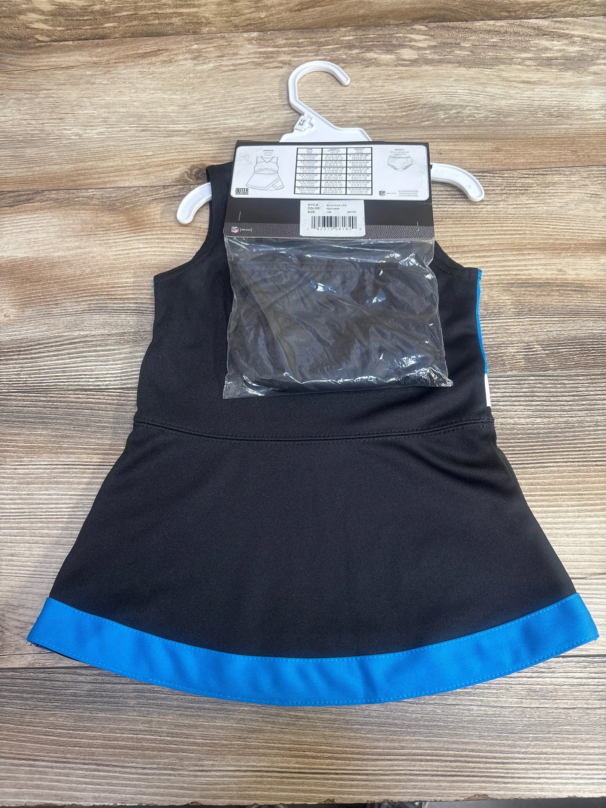 Black and blue cheerleader dress with attached black briefs on a white hanger over wooden background