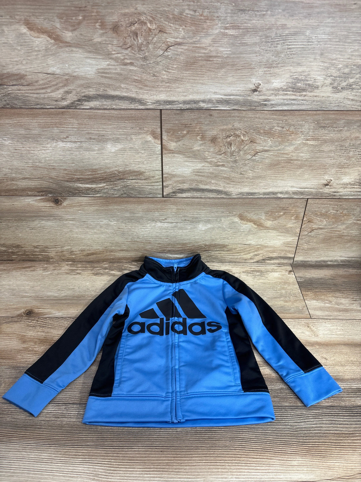 Children's blue and black Adidas zip-up jacket laid flat on wooden floor