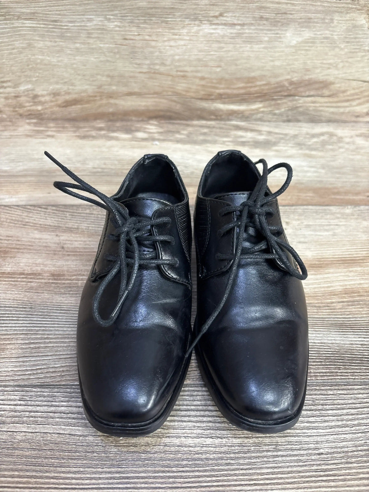 Top view of Bonafini Kids K-154 black leather dress shoes showing lace-up front and square toe on wooden floor