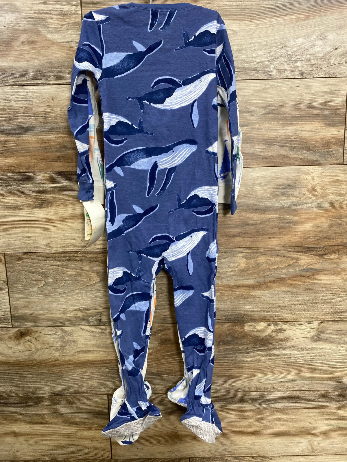 Blue baby onesie with white and dark blue whale print on wooden floor