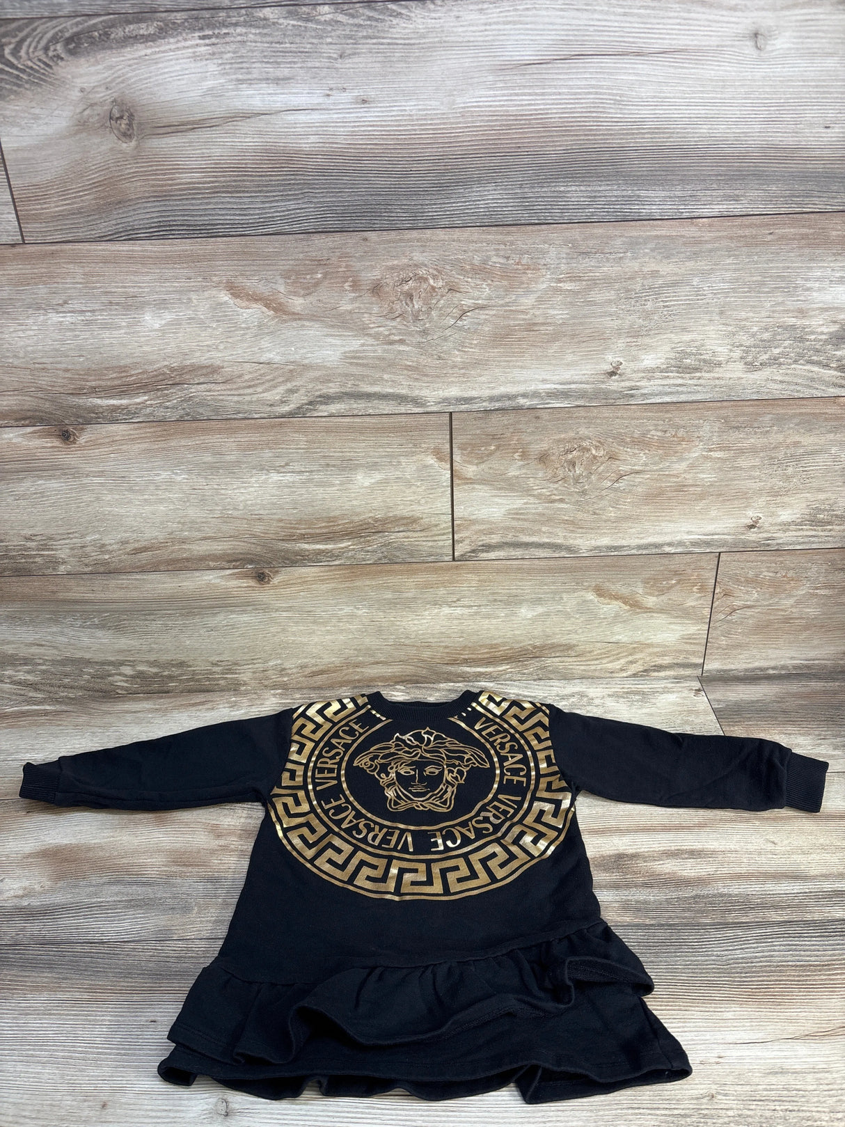 Black Versace children's dress with gold Medusa logo and Greek key pattern on wooden floor