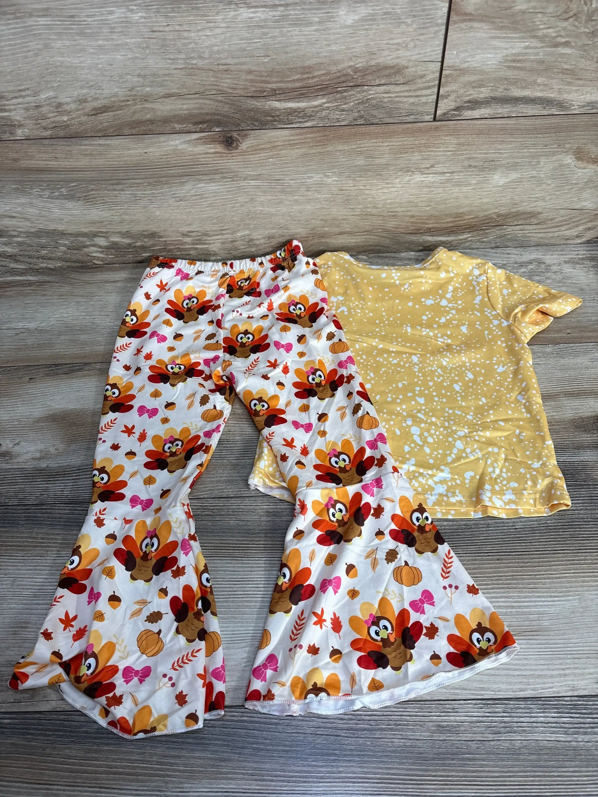 Kids Thanksgiving outfit with turkey print bell-bottom pants and yellow splatter top on wood floor
