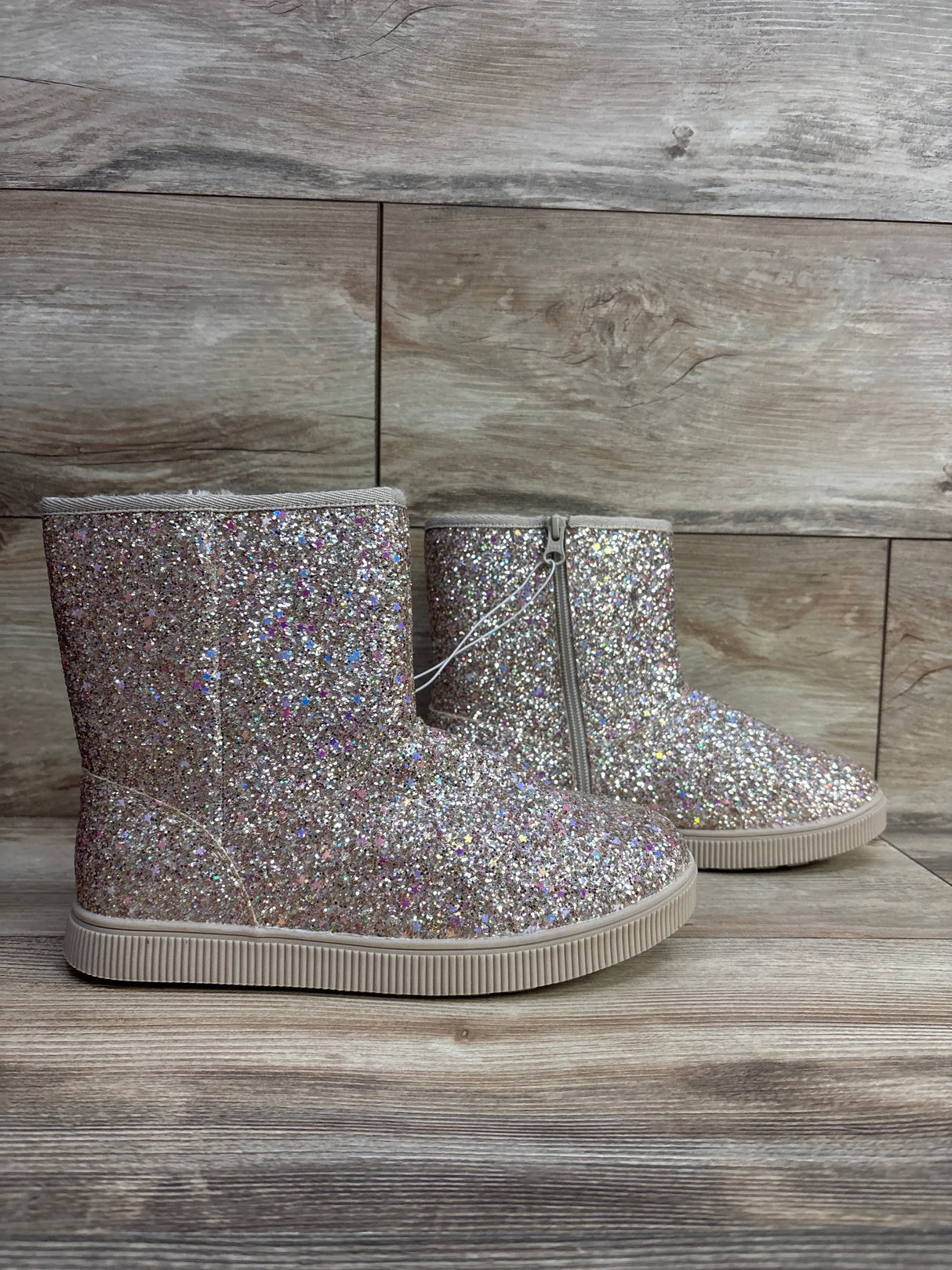 Children's glittery pink ankle boots with side zipper on wood background