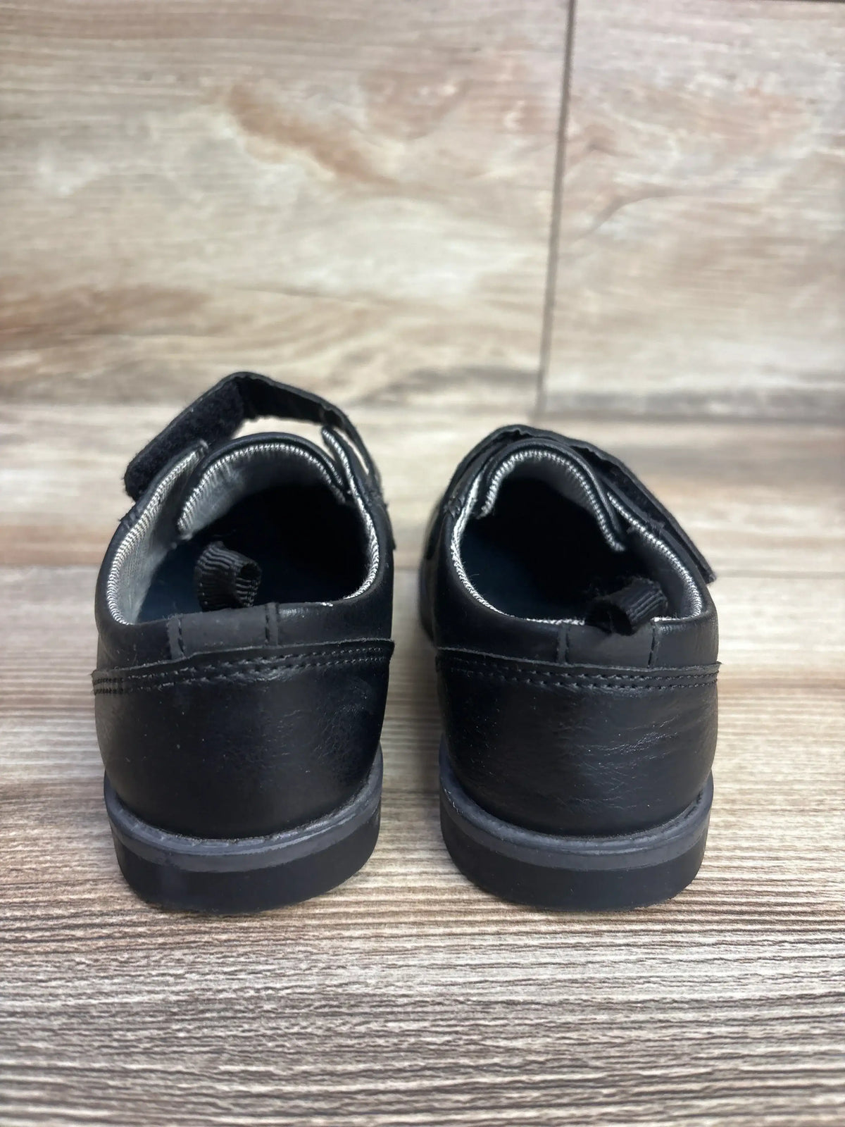 Back view of black toddler shoes with velcro straps on wooden floor, kids footwear resale