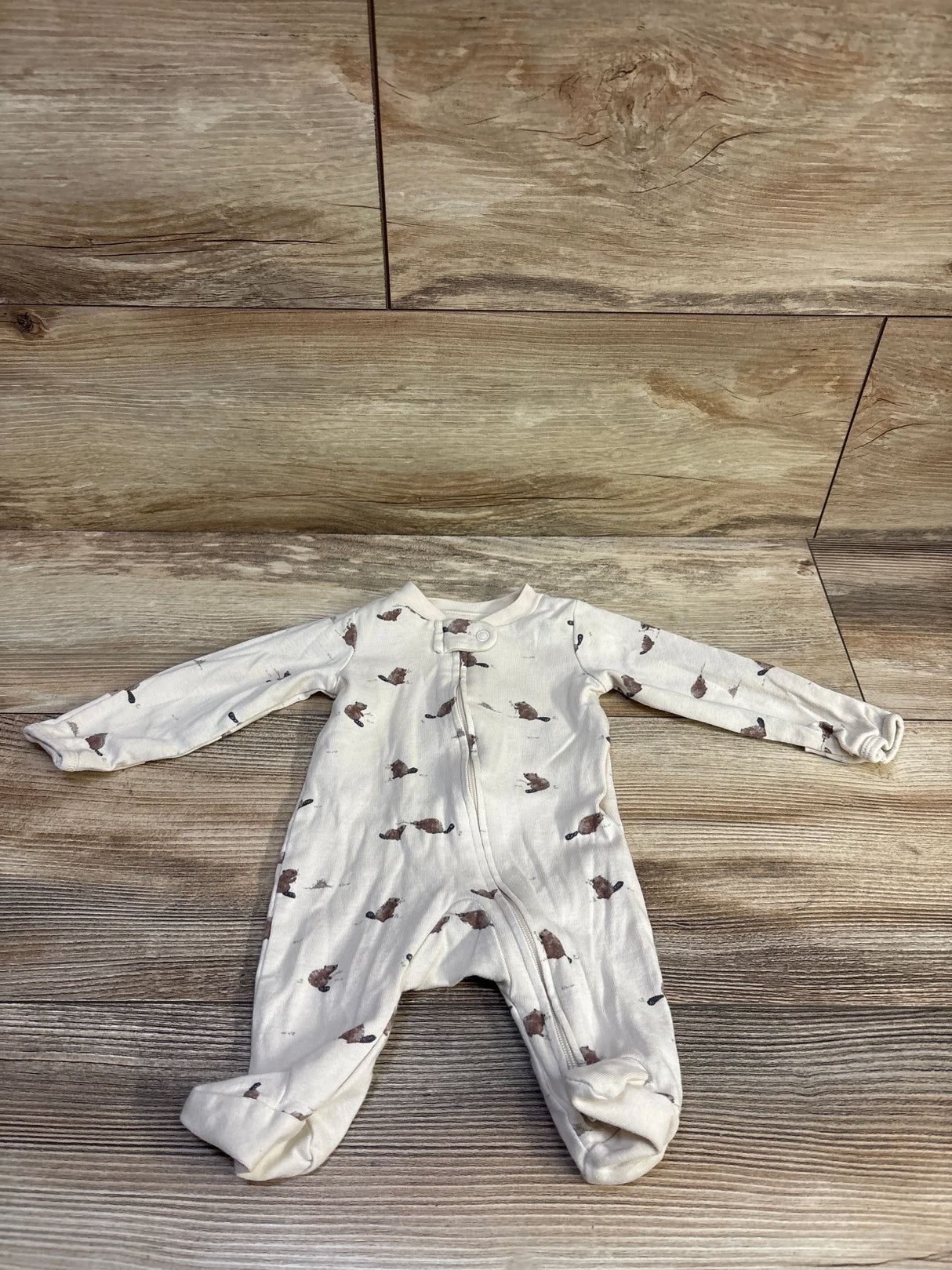 Flat-lay of Little Planet newborn organic sleeper with front zipper, footed legs, and brown animal print on wood background