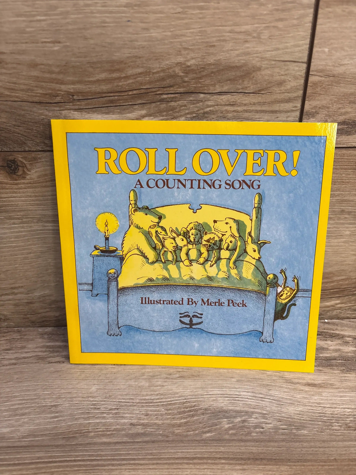 Front view of Roll Over! A Counting Song paperback showing yellow-bordered cover with animals in bed illustration on a wood background