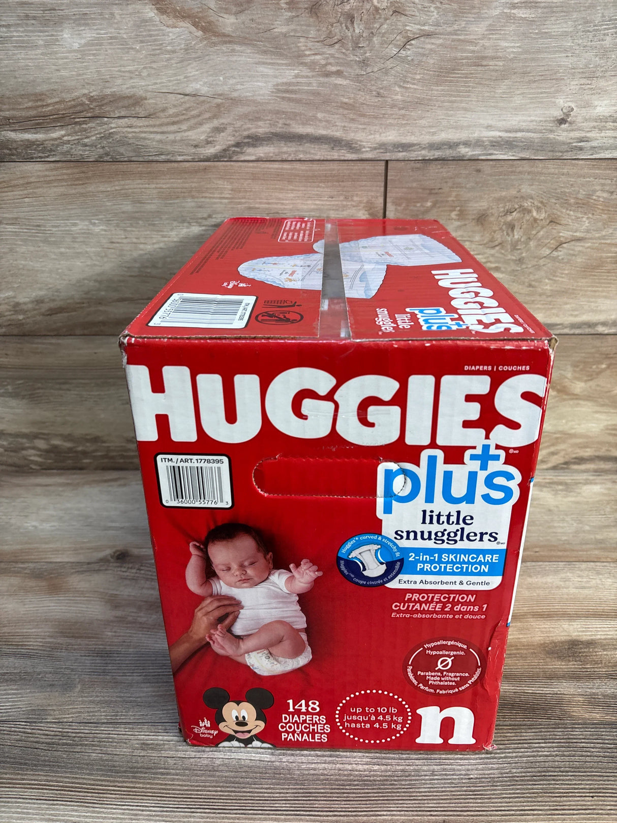 Huggies Plus Little Snugglers newborn diapers box, 148 count, red packaging, with baby image on wood background