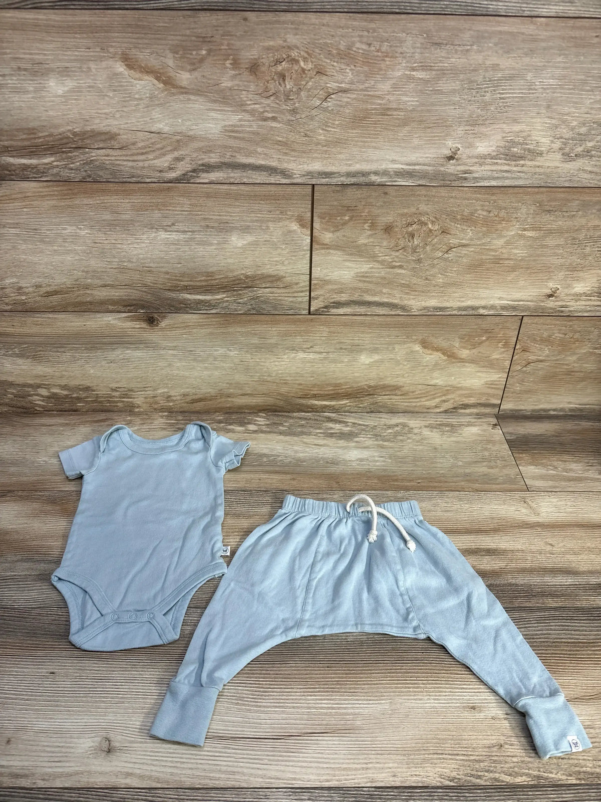 Flat lay of blue 2-piece baby bodysuit and pants showing snap crotch and drawstring waist on wood background