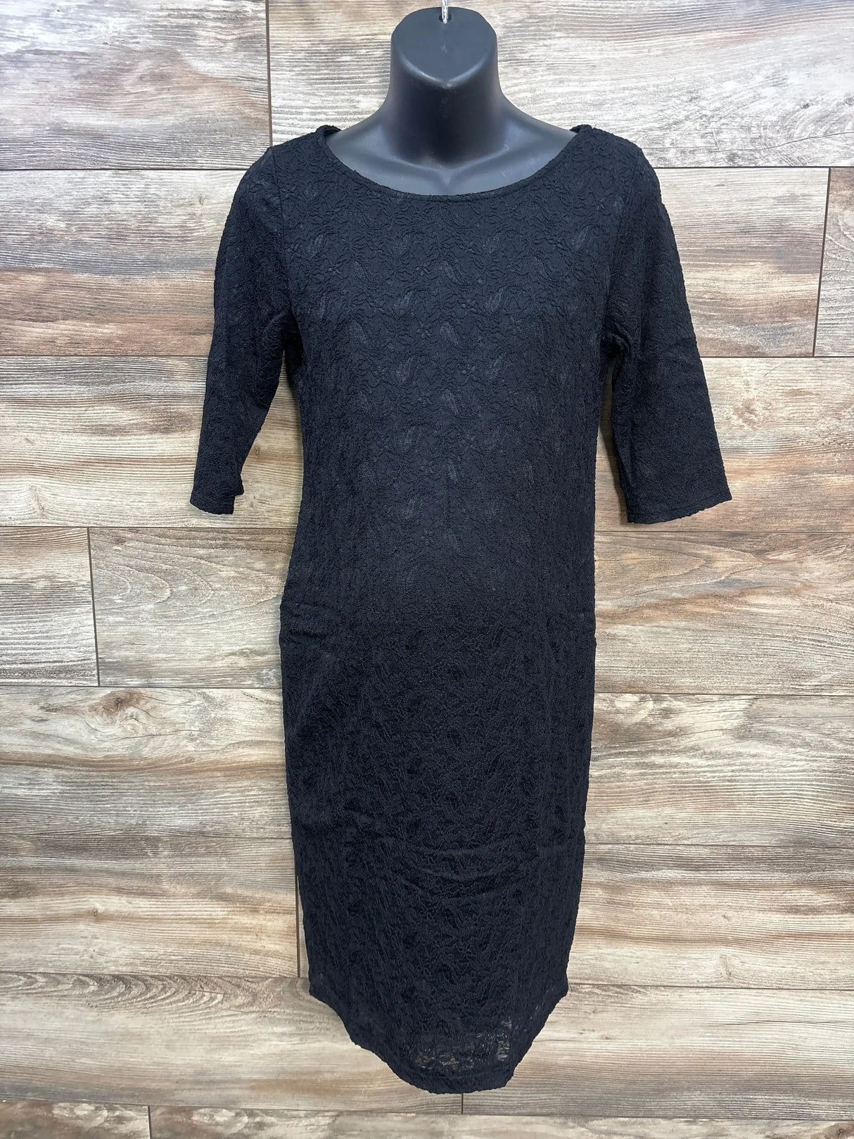 Front view of Pink Blush black lace fitted maternity dress with 3/4 sleeves on a mannequin against wood plank background