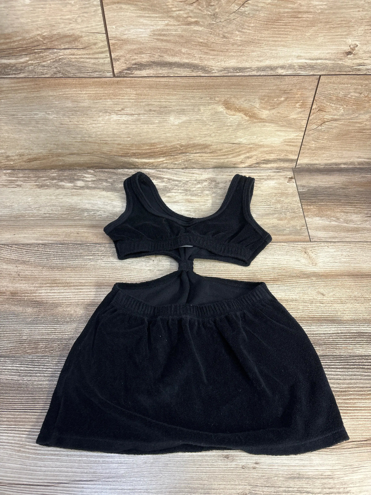Flat lay of black terry cloth one-piece toddler swim cover-up showing front knot cutout and elastic waist on wood floor