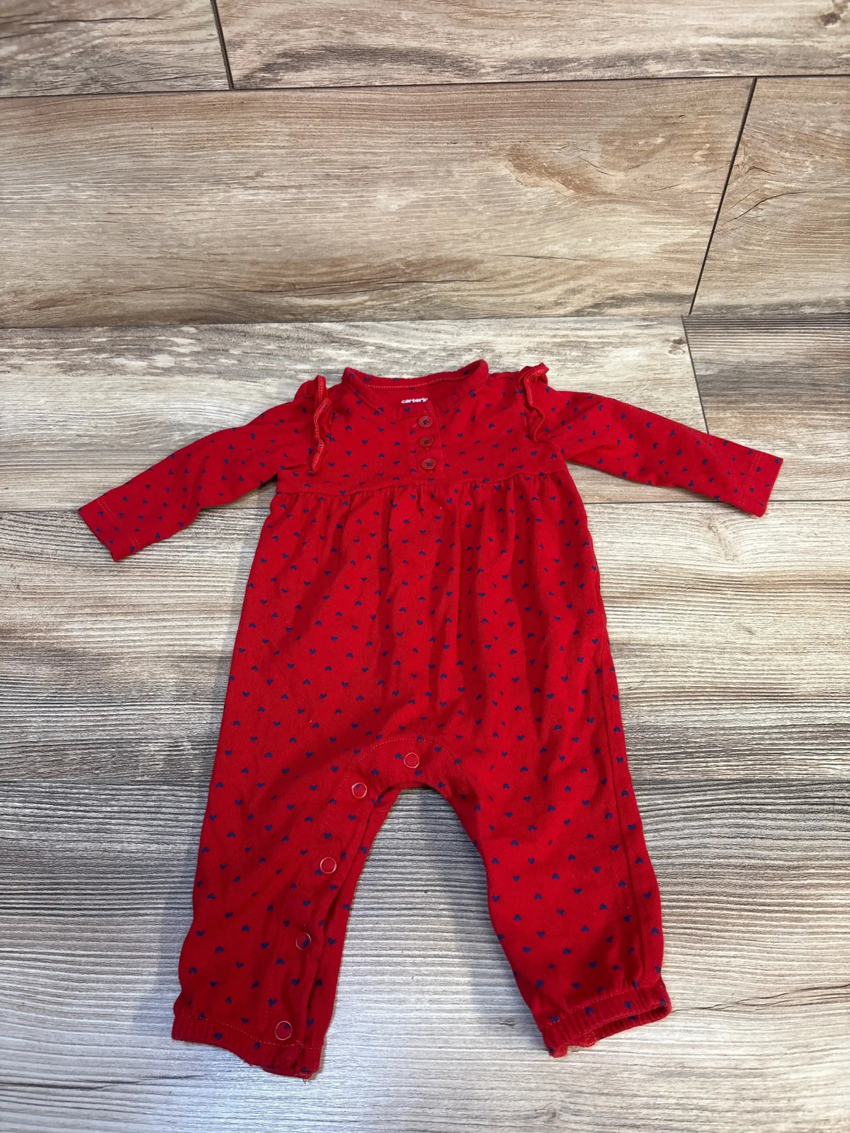 Flat lay of Carter’s Hearts Romper, red size 3M, with navy hearts, shoulder ruffles, and crotch snaps on wood