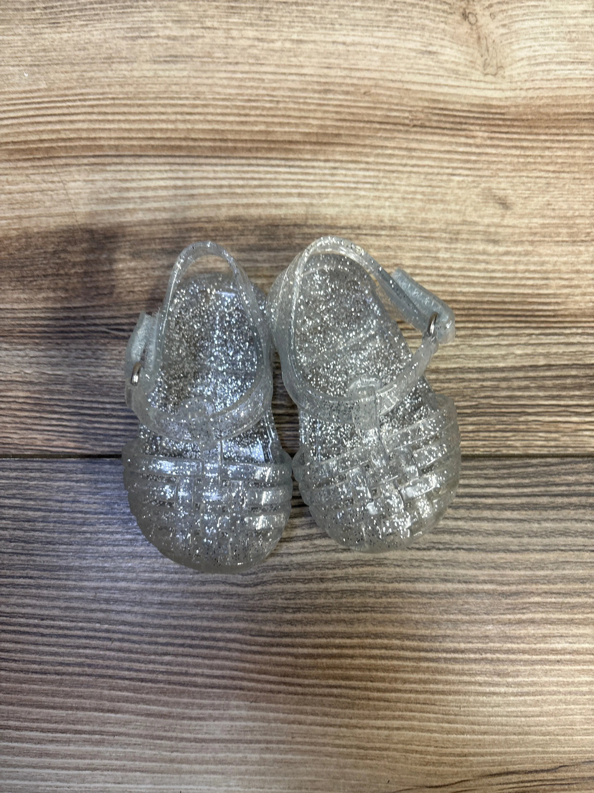 Top-down view of toddler Old Navy clear glitter jelly sandals with ankle straps on woodgrain background