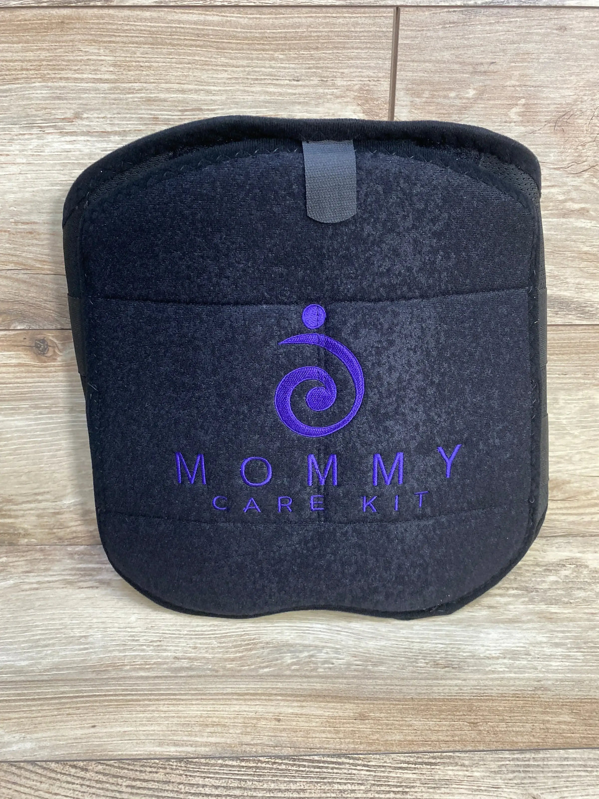 Front of Mommy Care Kit back support belt showing purple embroidered logo and Velcro tab on wood floor