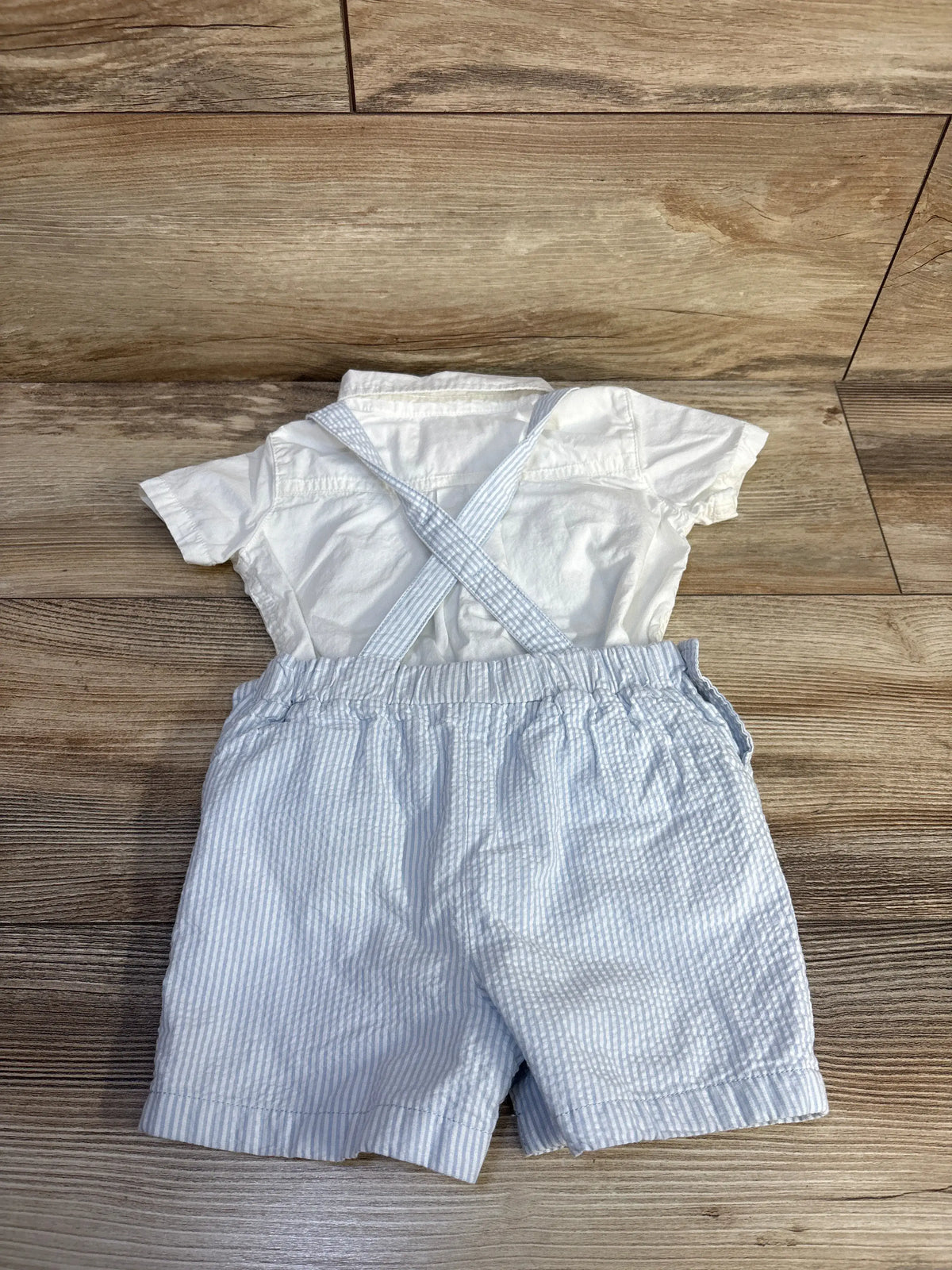 Top view of Tommy Bahama outfit set showing white polo bodysuit and blue and white striped shortalls with crossed straps on wood floor