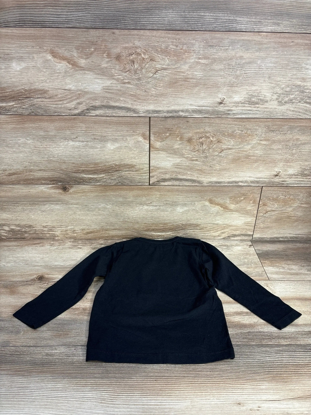 Back view of Bonpoint Star Boy shirt, black 3T, showing long sleeves and plain back on wood floor