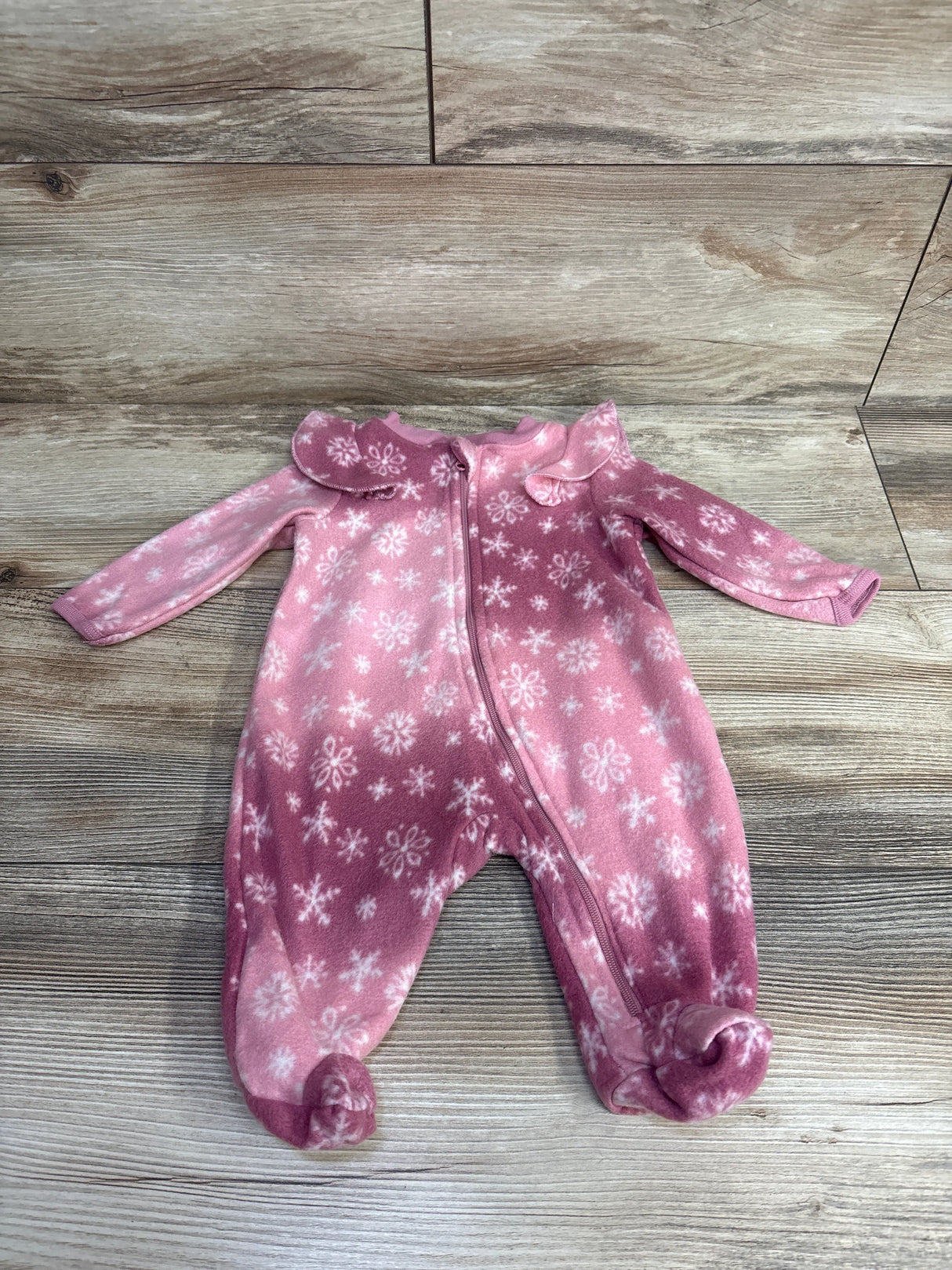 Pink baby fleece onesie with white snowflake pattern and zipper, laid on wooden floor