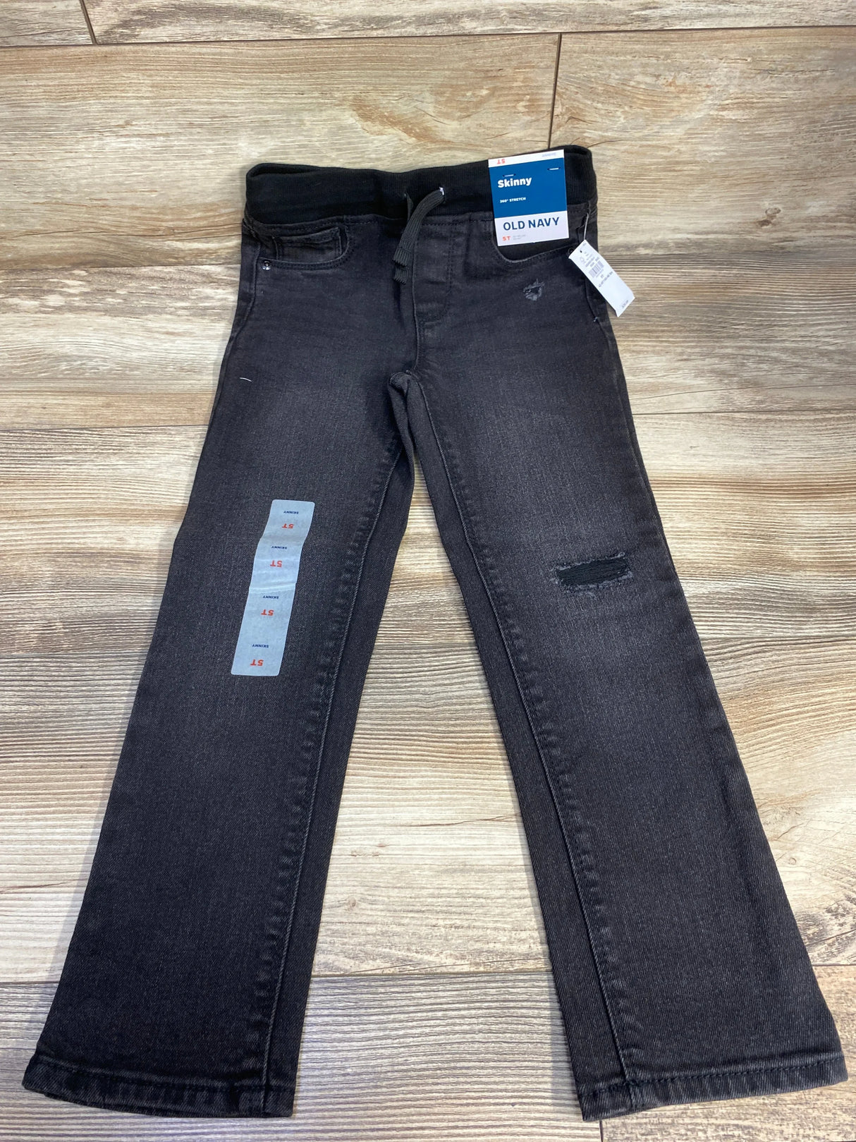 Black Old Navy skinny jeans for kids with elastic waist and toddler size tag, on wood floor