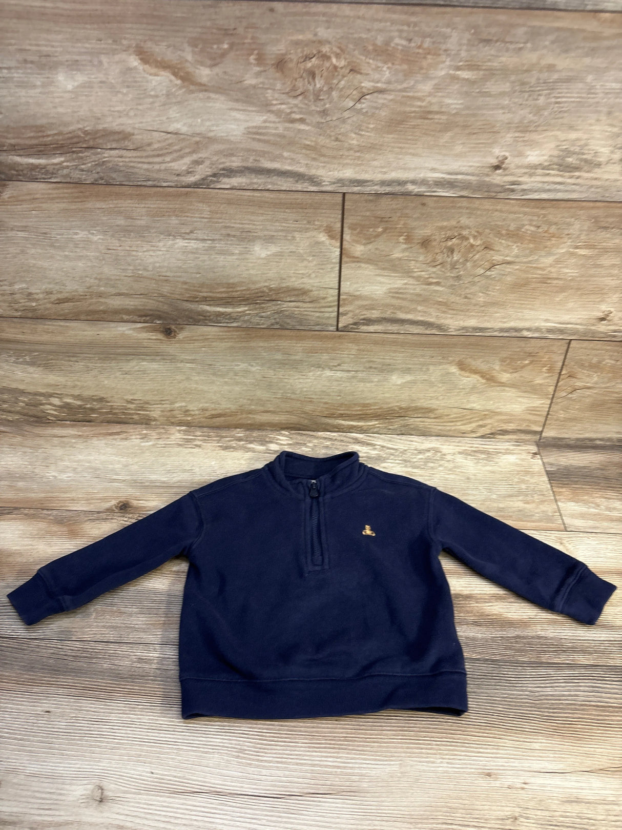 Front view of Baby Gap navy quarter-zip pullover showing half-zip collar and small embroidered logo on wood floor background