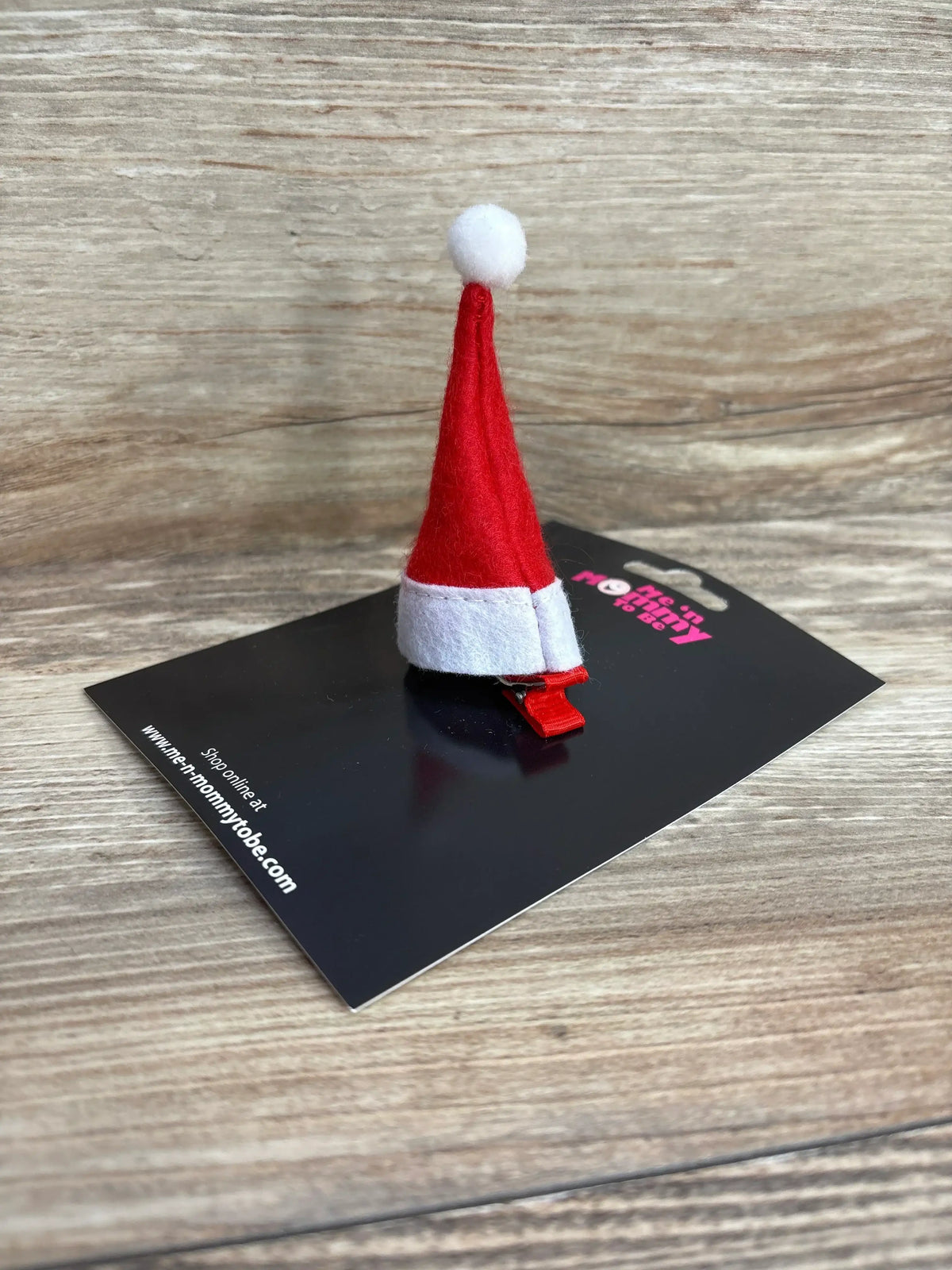 Red and white Santa hat hair clip for kids, festive holiday accessory on black card