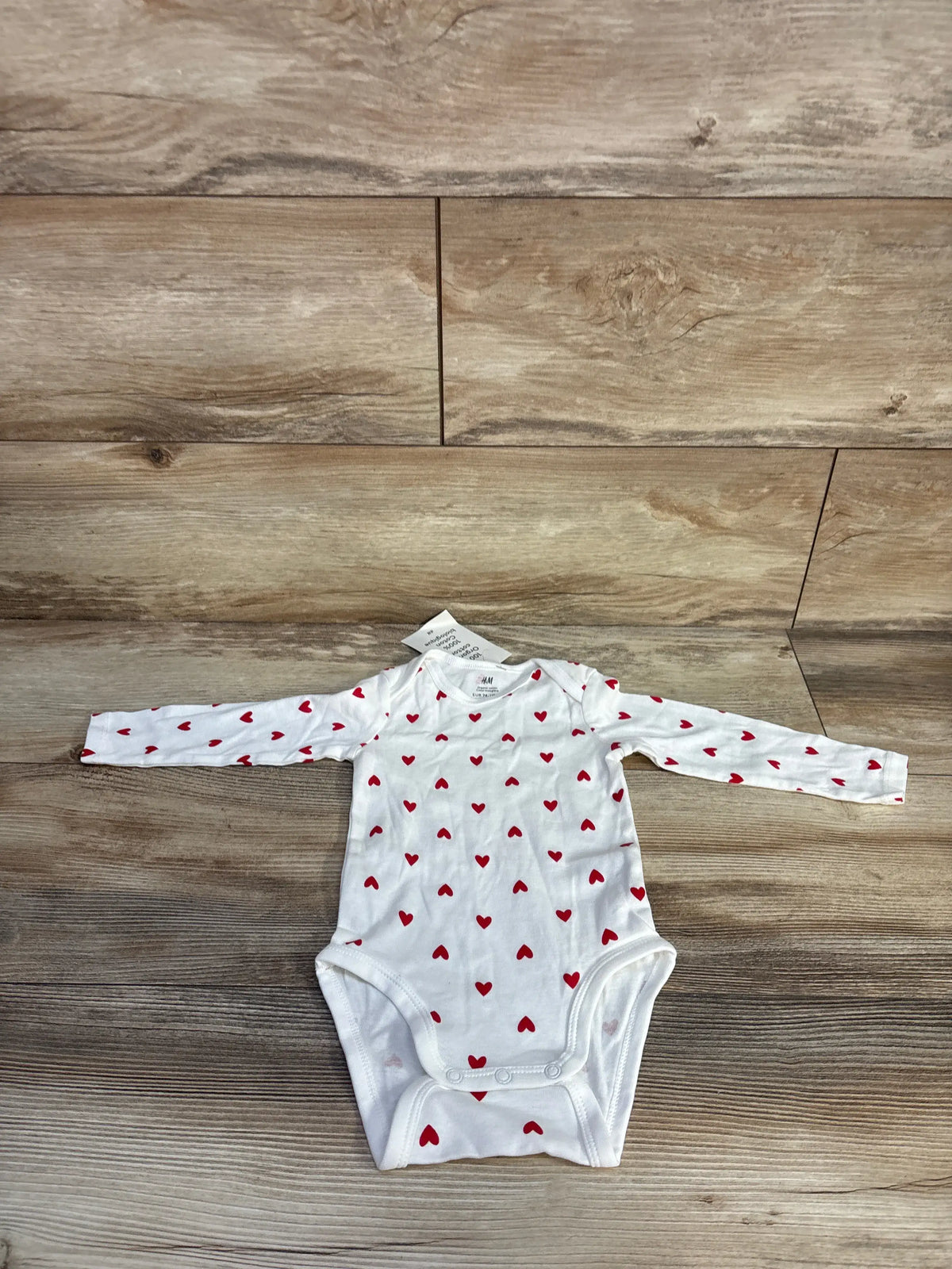 Front view of H&M white long sleeve bodysuit size 9 months showcasing red heart print with wood background