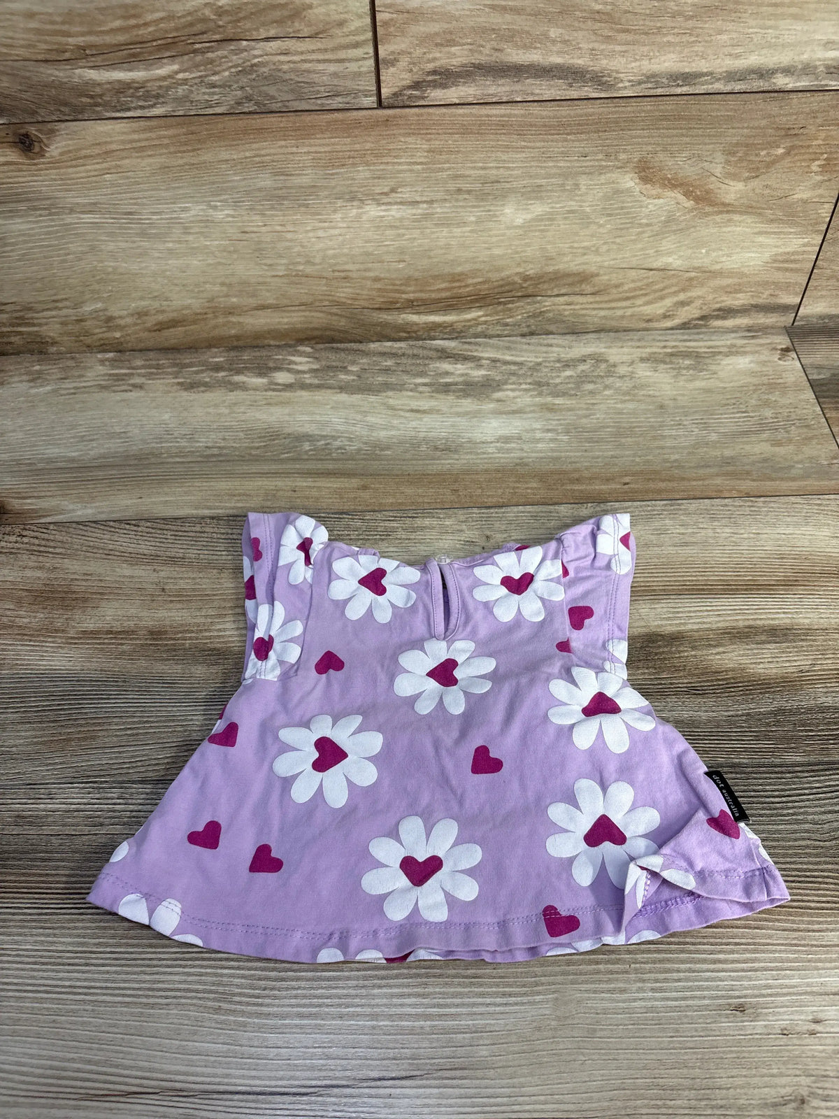 Front view of Dot Australia purple flutter sleeve shirt for 3-6 months with white flowers and magenta hearts on wood background