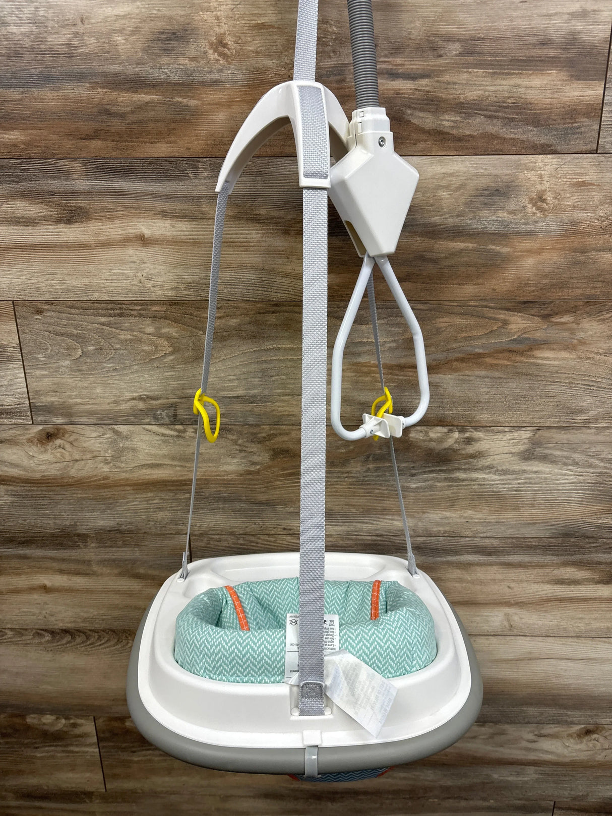 Front view of Graco Doorway Bumper Jumper Caravan with mint green seat, gray safety straps, yellow hooks, white frame on wood background