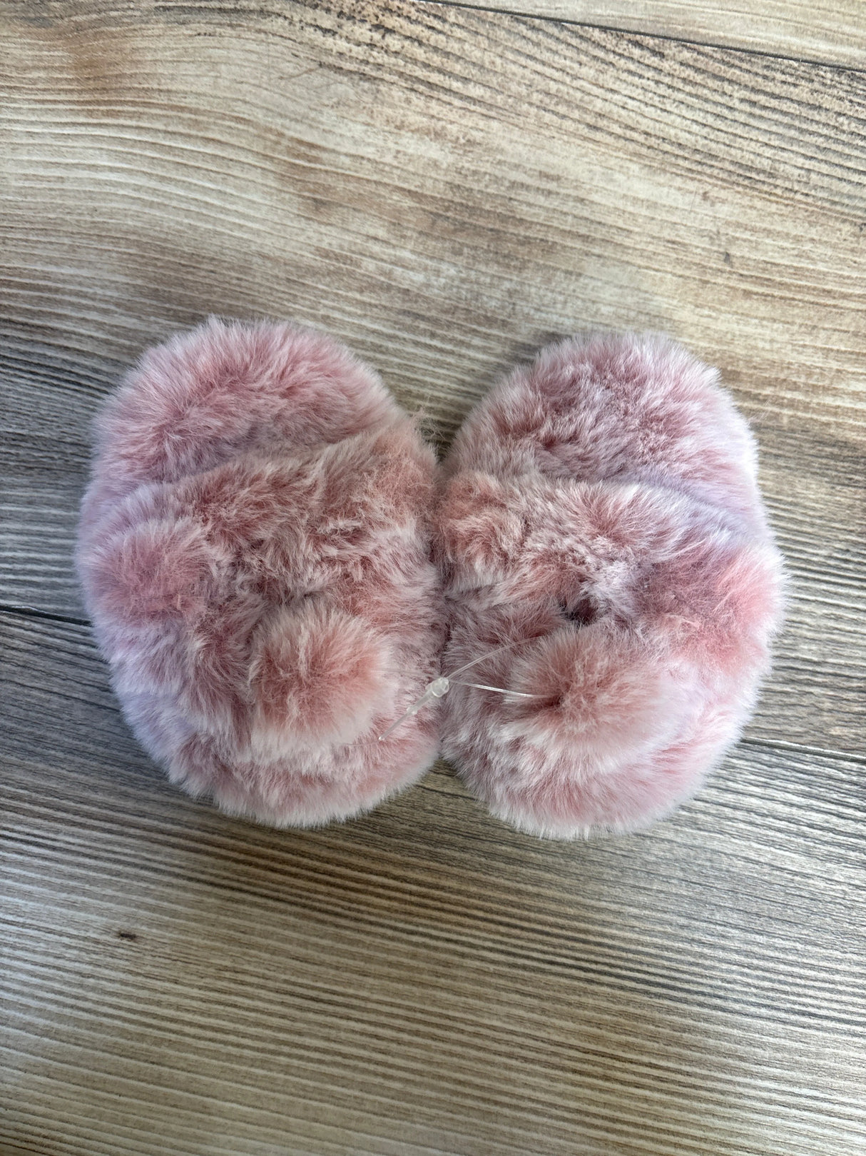 Plush pink fuzzy baby slippers on a wood background, cozy toddler footwear