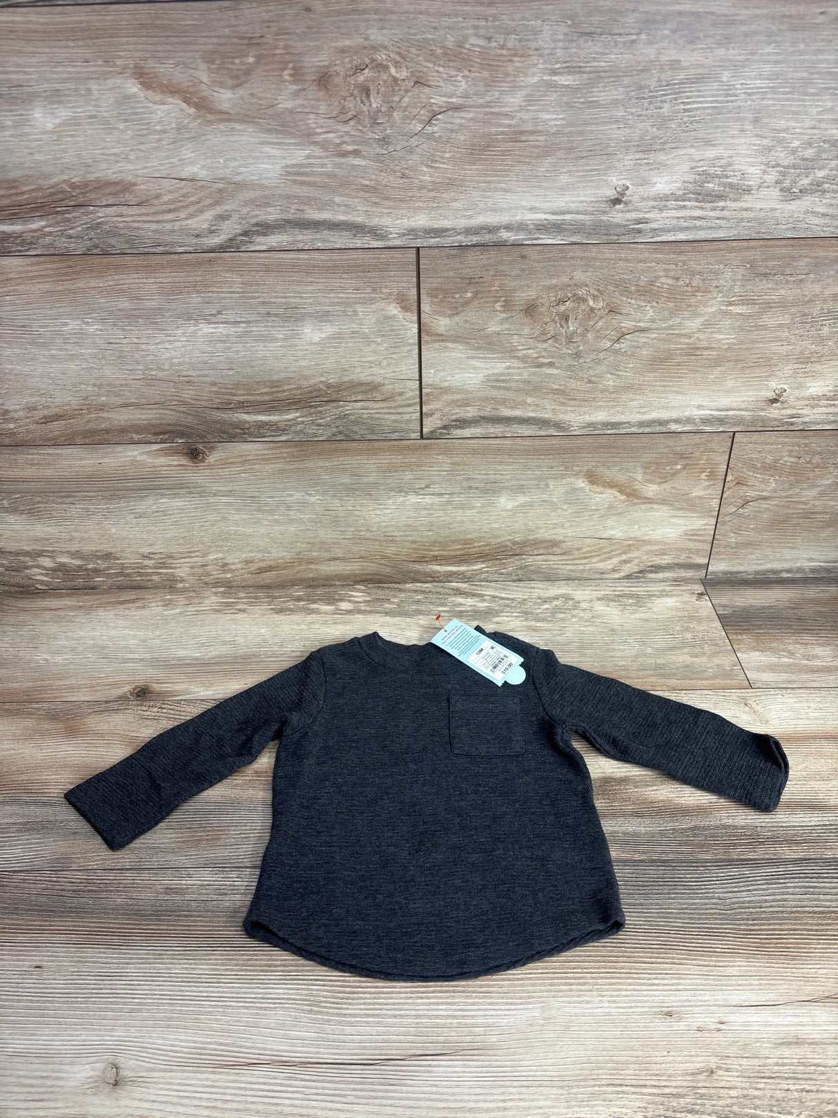 Dark gray long sleeve toddler shirt with chest pocket and tag on wood background