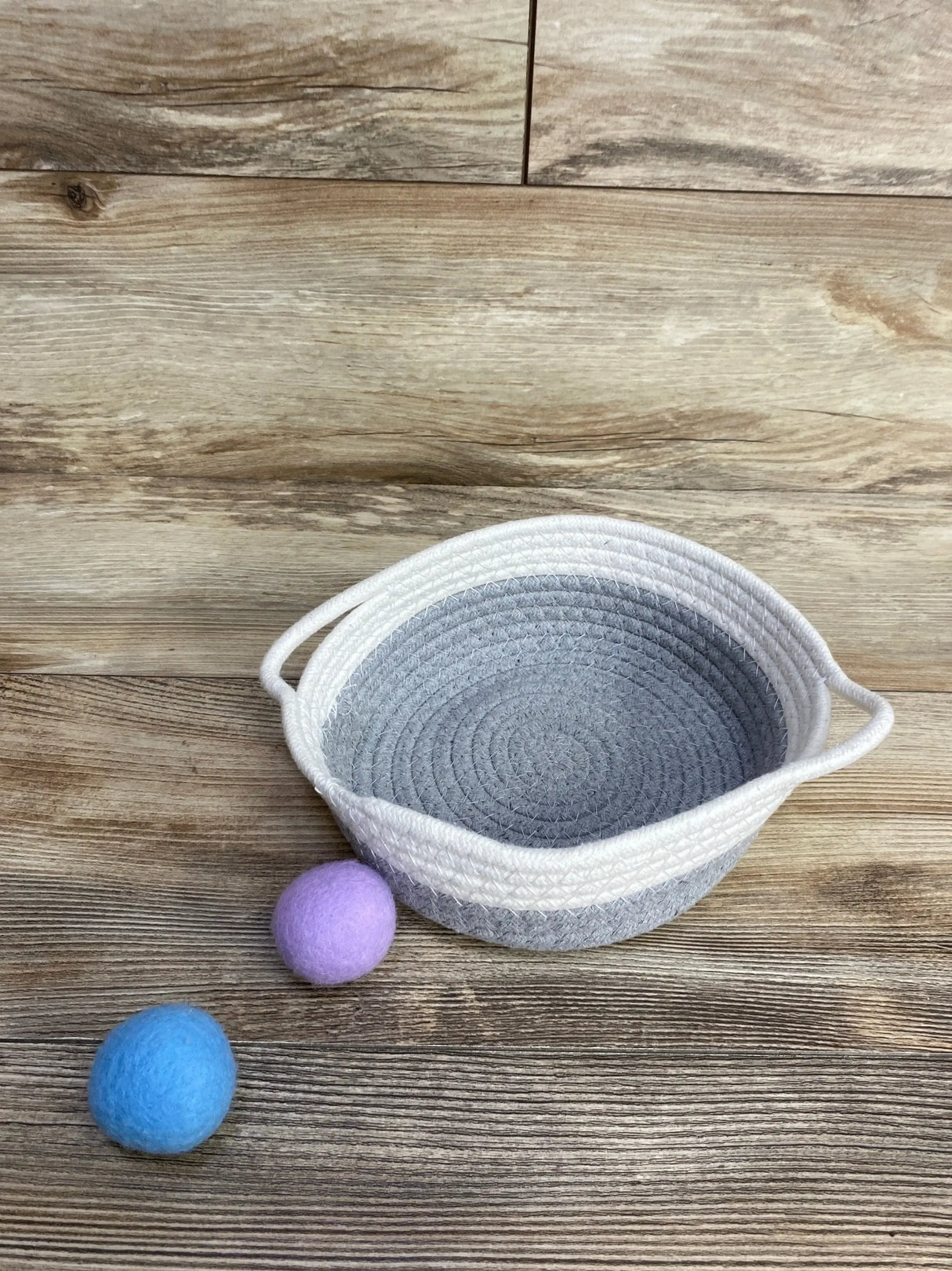 Gray and white woven basket with handles and two felt balls on wood background