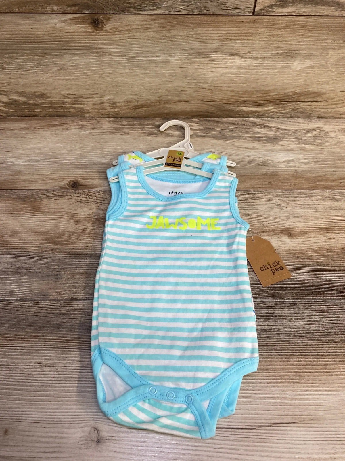 Front view of blue and white striped baby tank bodysuit with neon yellow ‘JAWSOME’ print and snap closures on wooden background