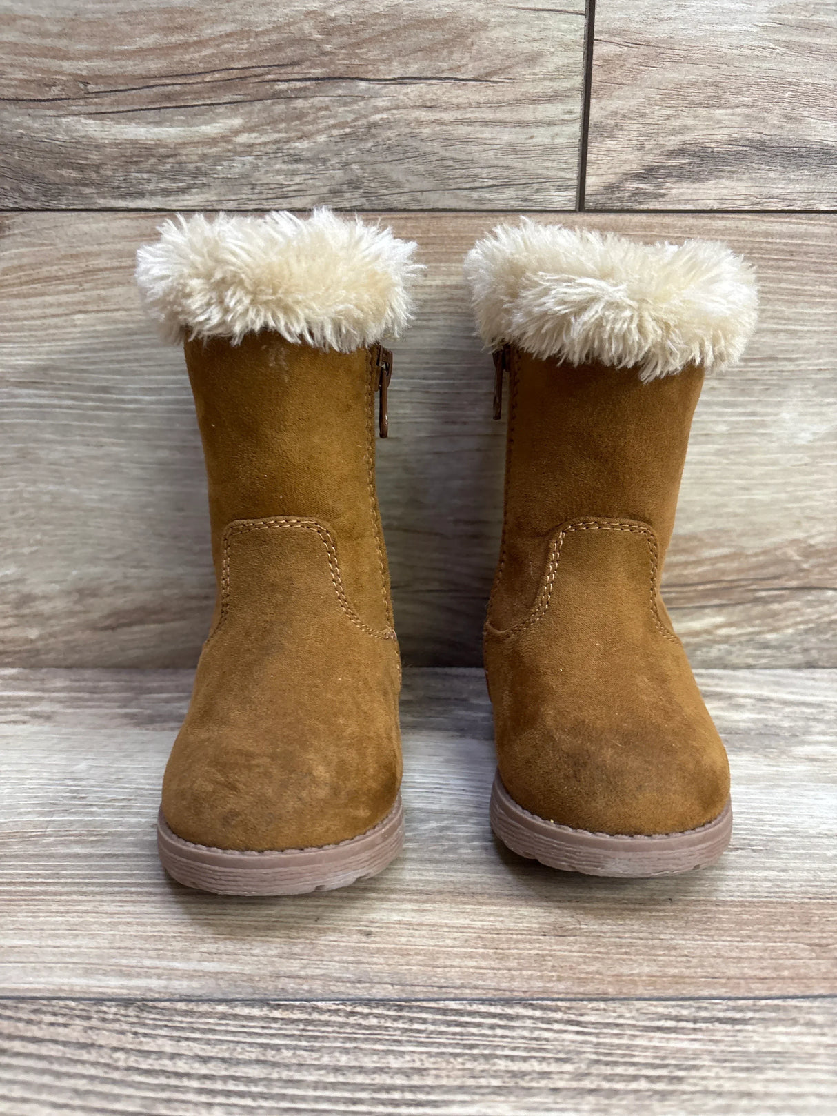 Pair of brown toddler boots with fluffy cream-colored lining on wooden floor background