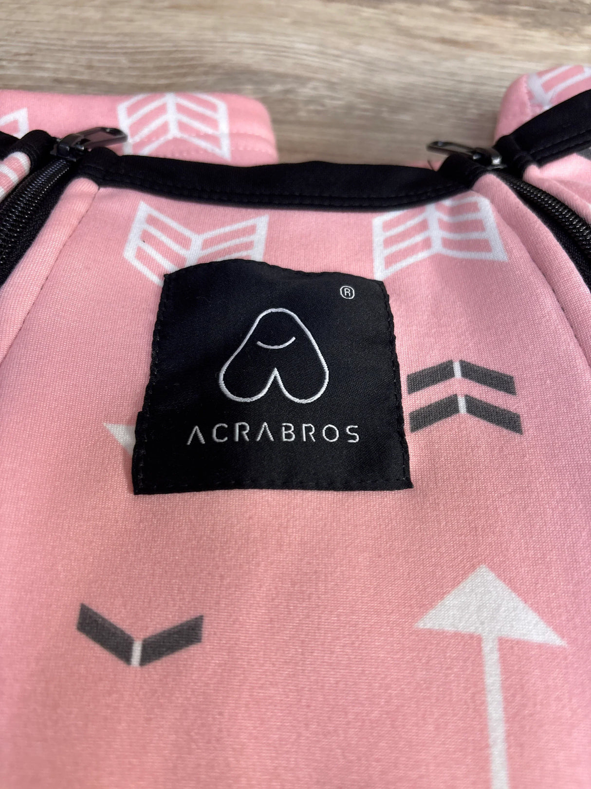 Pink ACRABROS baby carrier fabric with white arrow pattern and black logo tag