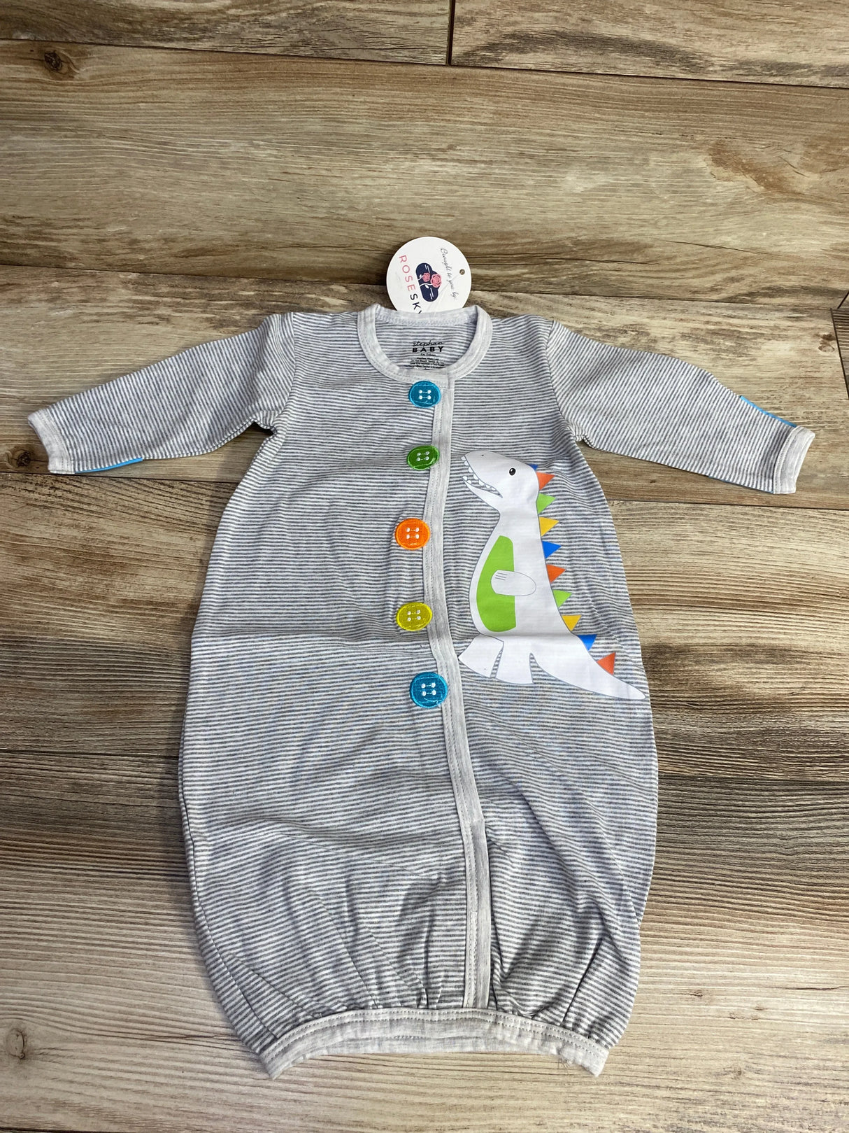 Gray striped baby sleeved sleeper with colorful buttons and cute dinosaur graphic on wood background