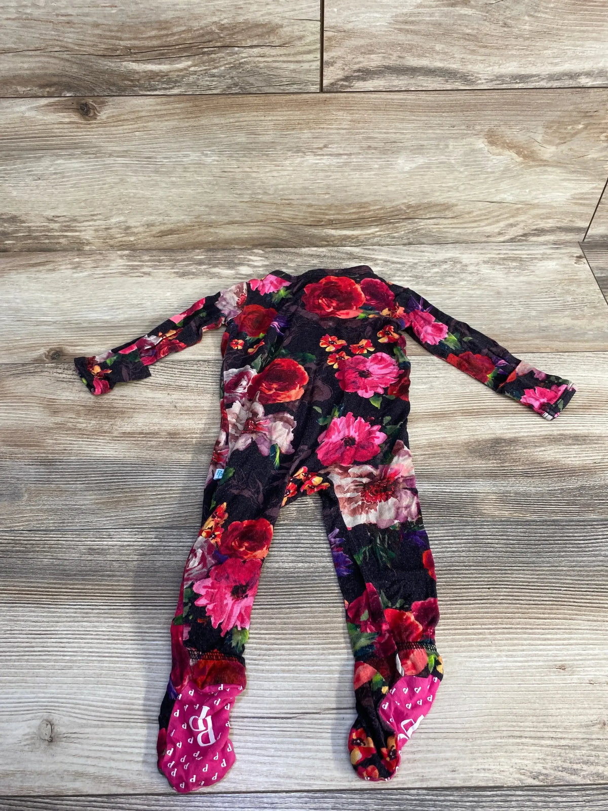 Flat lay of newborn black floral footie with red and pink roses, long sleeves and built-in feet on wood background