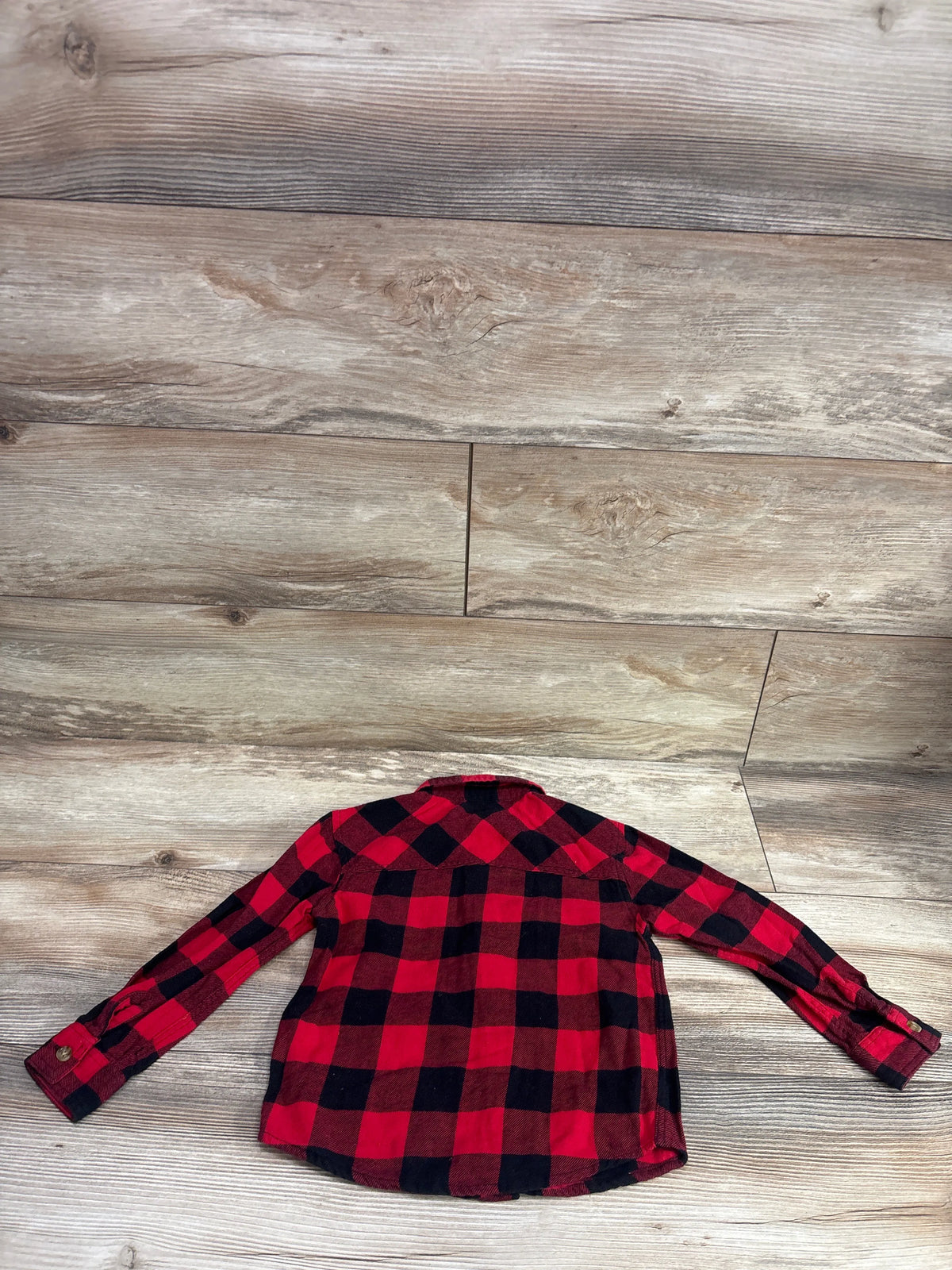 Red and black buffalo plaid button-up flannel shirt for toddlers on a wooden background.