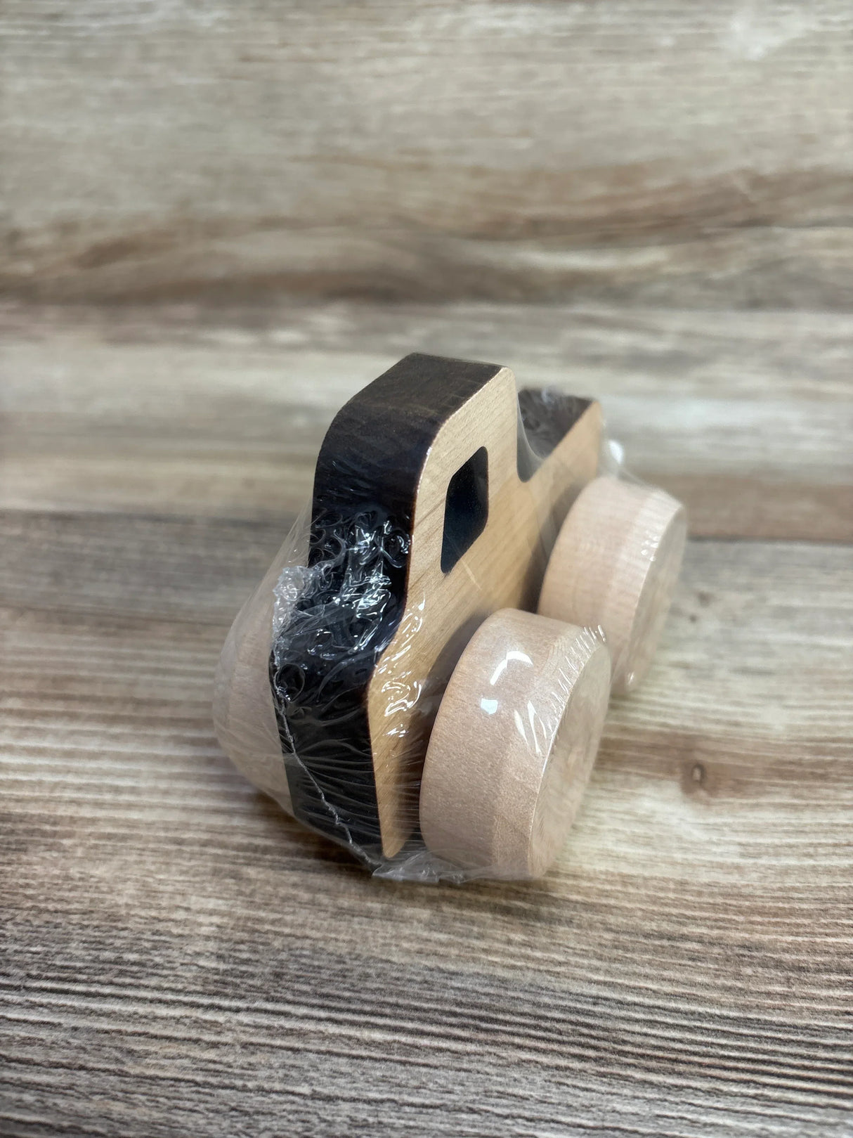 Three-quarter view of Mini Monster Pickup wooden car showing natural maple body, black roof, round wheels, wrapped in plastic on wood surface