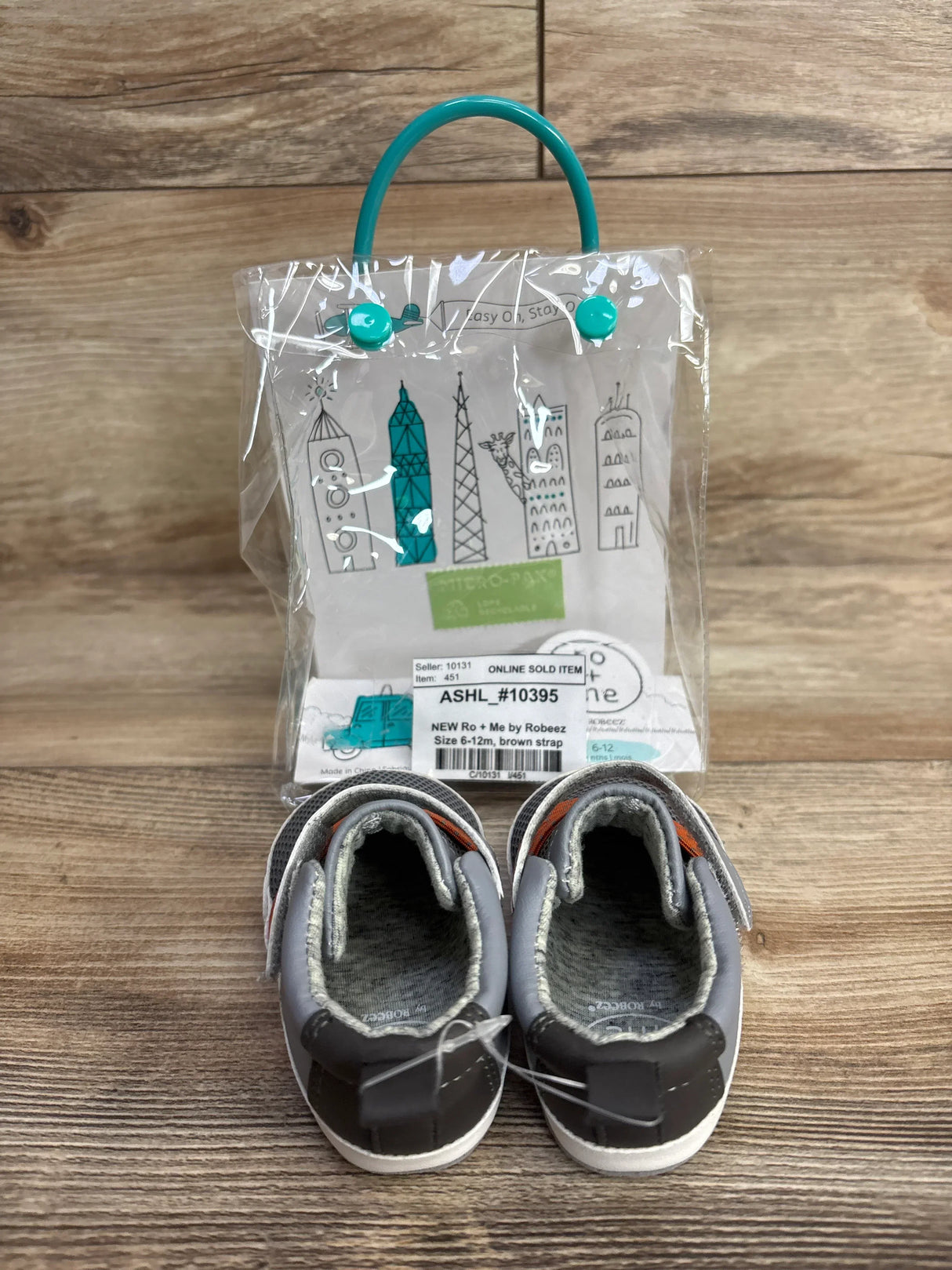 New Ro + Me by Robeez gray baby shoes with brown strap, size 6-12 months, displayed with clear packaging featuring cityscape design
