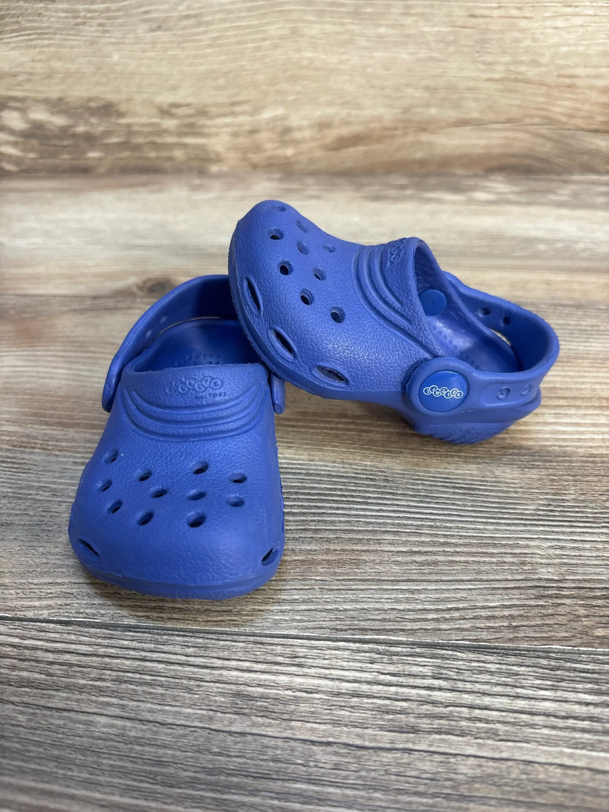 Three-quarter view of Crocs Classic Clog in blue showcasing ventilation holes, heel strap and textured footbed on wood surface