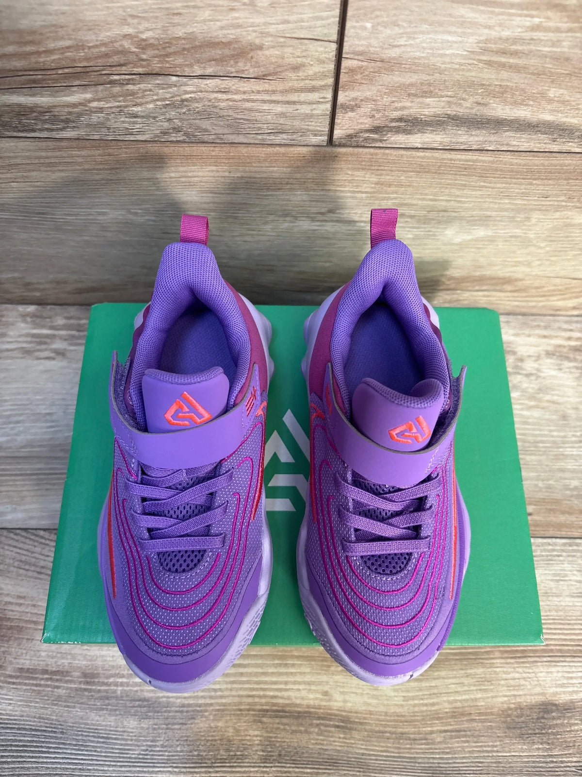 Top view of Nike Giannis Immortality 4 PS Black Raspberry kids sneakers showcasing purple and pink mesh upper, Velcro strap, and cushioned sole on green shoebox and wood floor