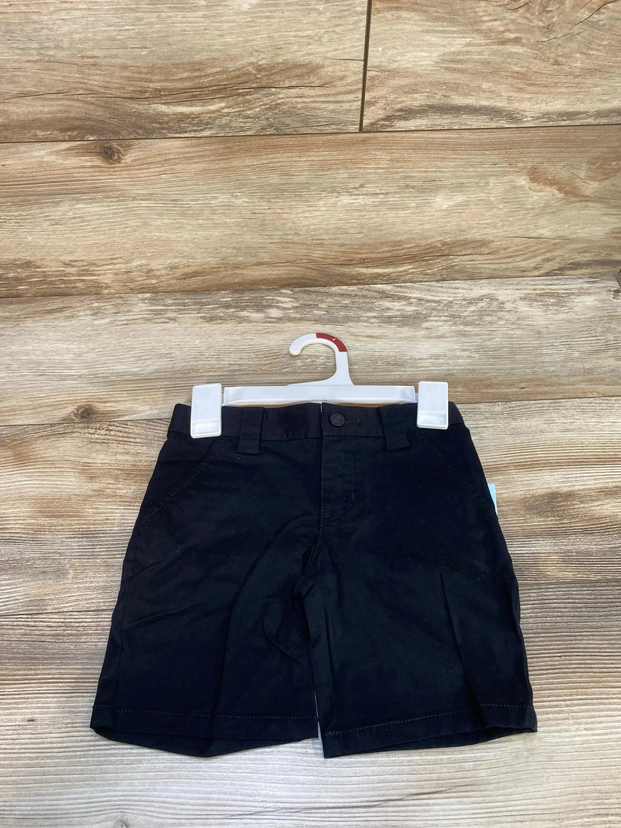 Front view of Cat & Jack toddler black uniform shorts with button-and-fly waist, belt loops and side pockets on wood background