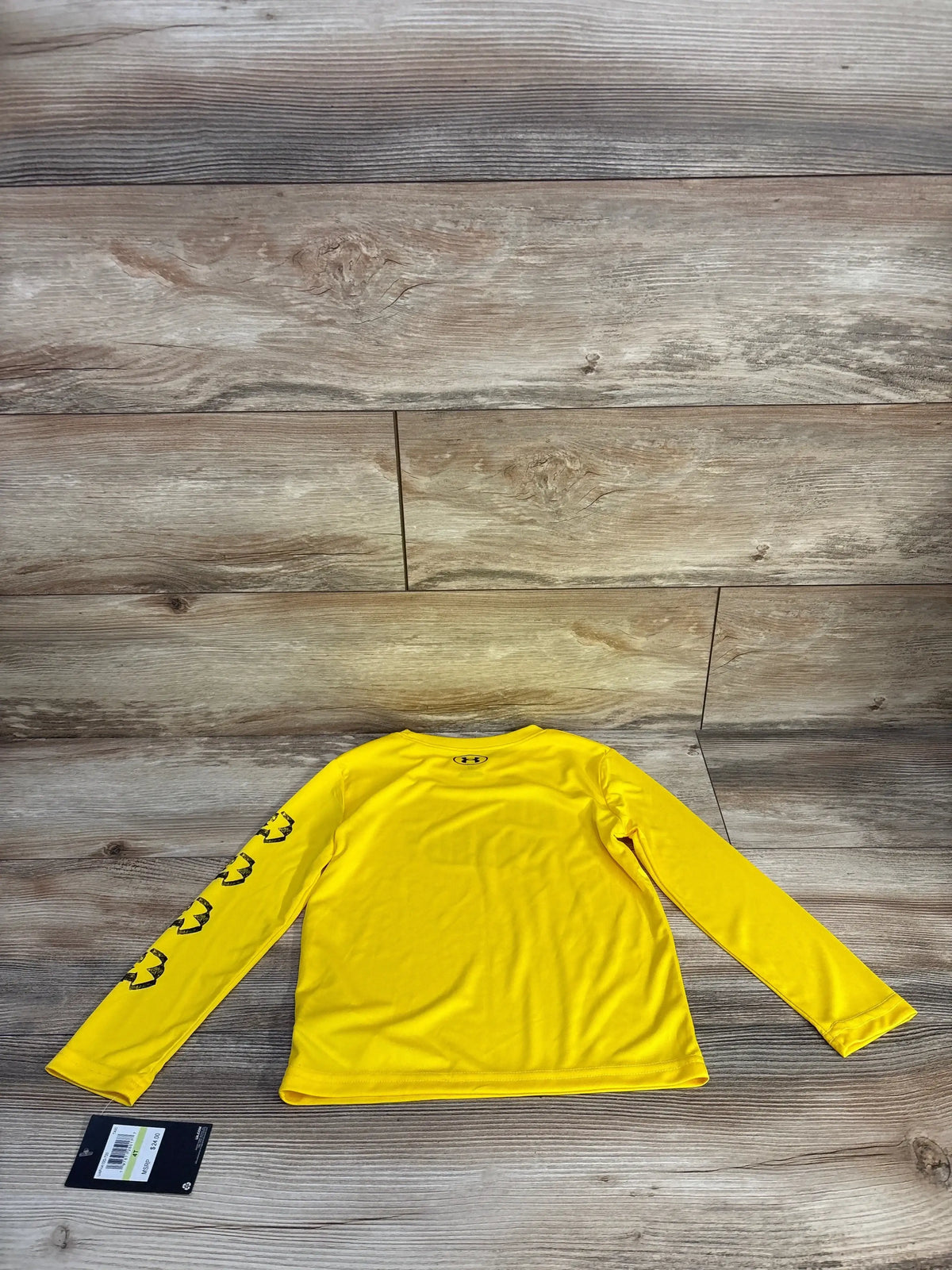 Back view of Under Armour long sleeve shirt in yellow showing logo at back neck and black UA sleeve graphics on wood